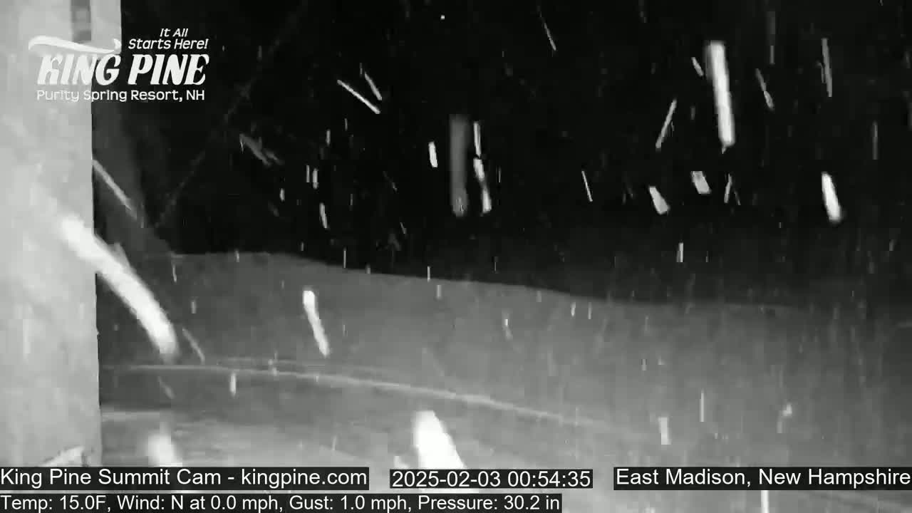 Snow falls at night in a dimly lit outdoor area.