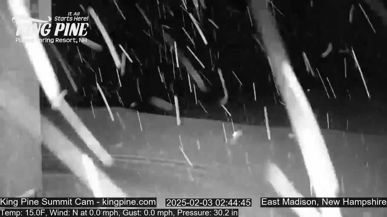 A nighttime, snow-filled scene shows falling snow in front of a dark surface.