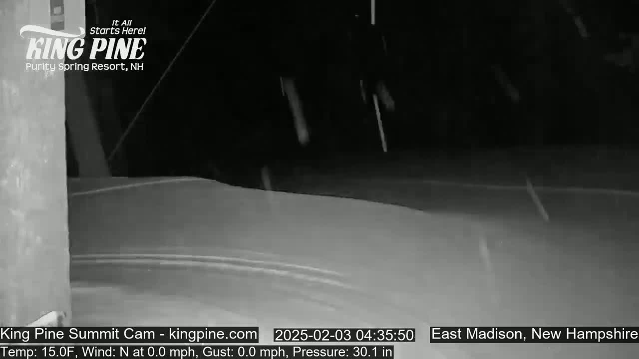 A nighttime, snow-covered scene shows light snowfall in the distance.
