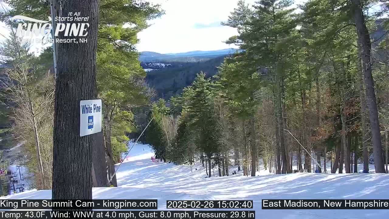 A snowy ski slope nestled among evergreen trees on a sunny day with a temperature of 43°F and a WNW wind.