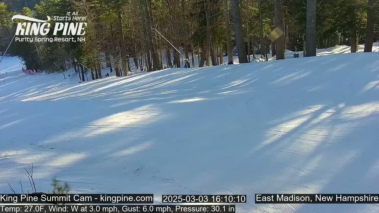 A snow-covered ski slope in a sunny, wooded area with a light westerly wind.