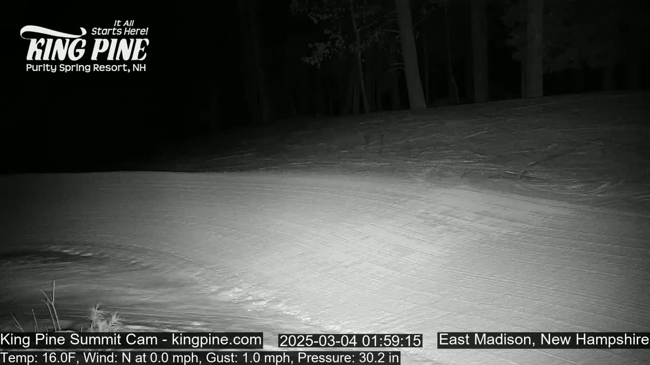 A snow-covered slope at night, under a dark sky, is illuminated by an artificial light source.
