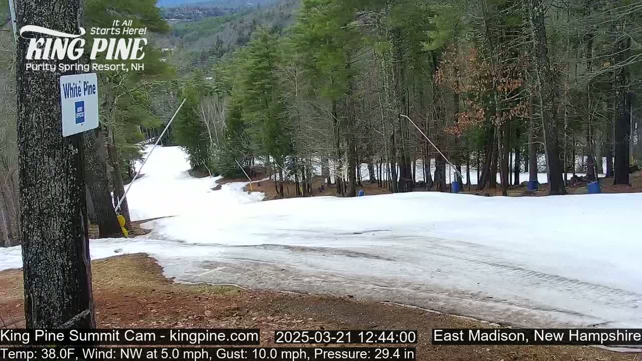 A snow-covered ski slope in a wooded area with a partly cloudy sky.