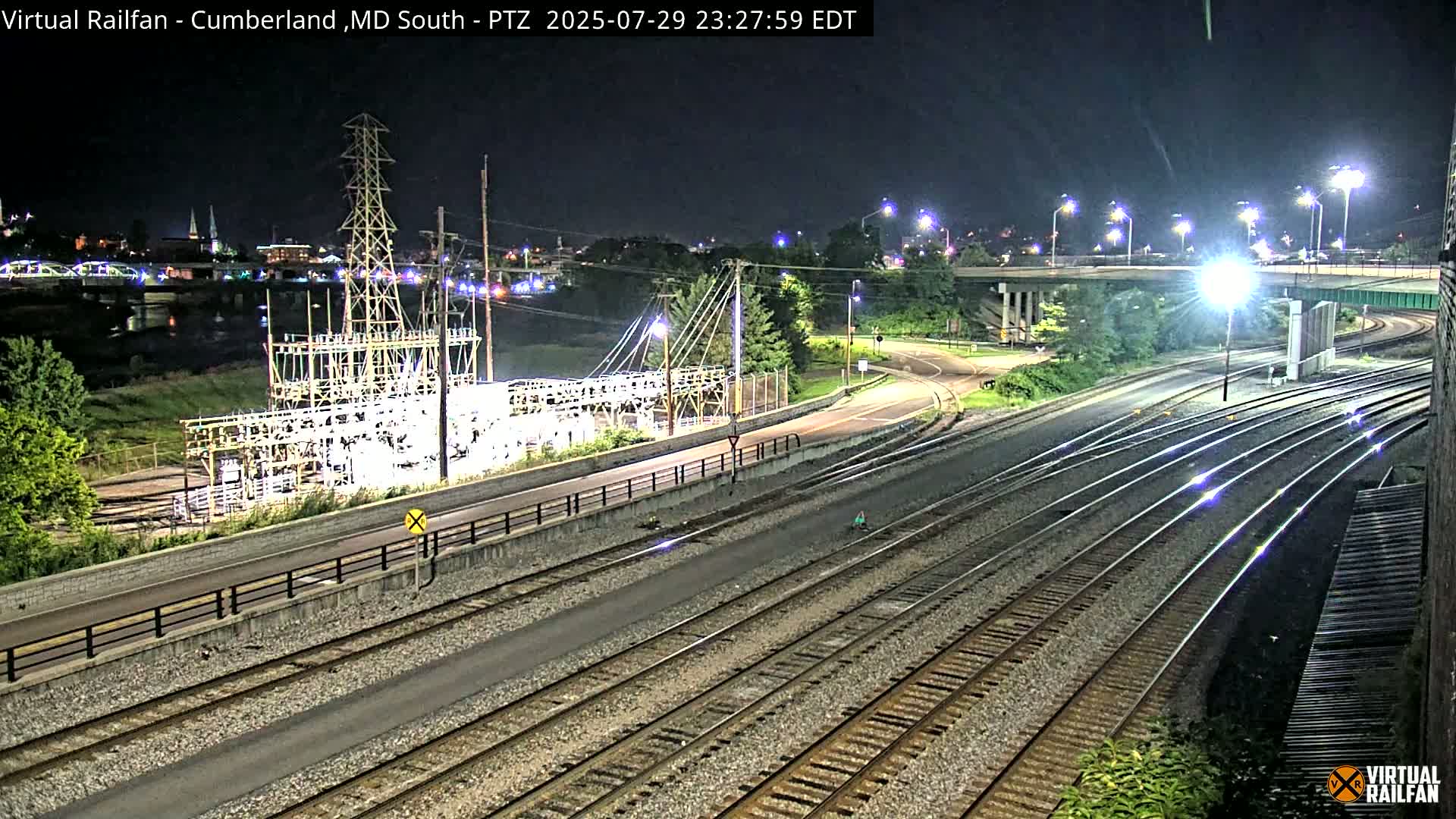 A nighttime view of railroad tracks intersecting with roads and a power substation, under clear skies.