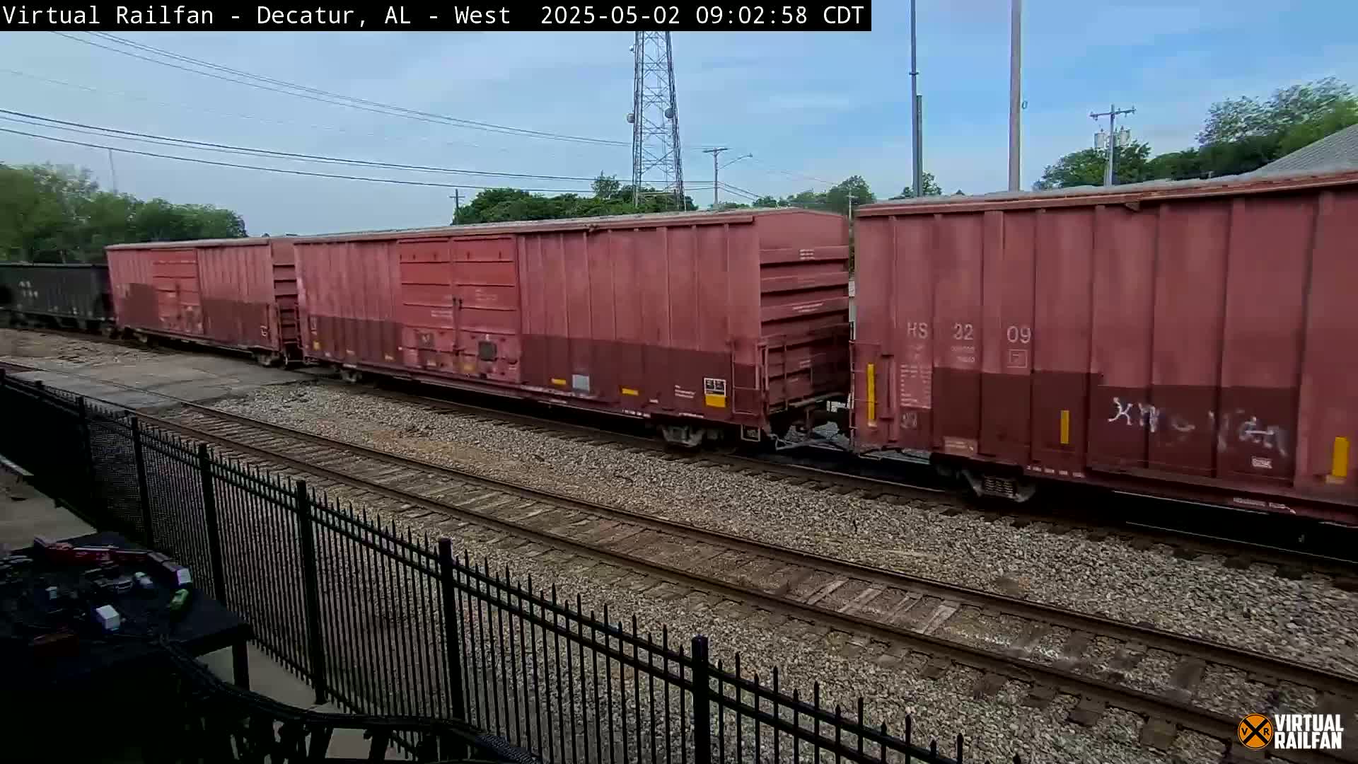 A long freight train of red boxcars moves along train tracks on an overcast day.