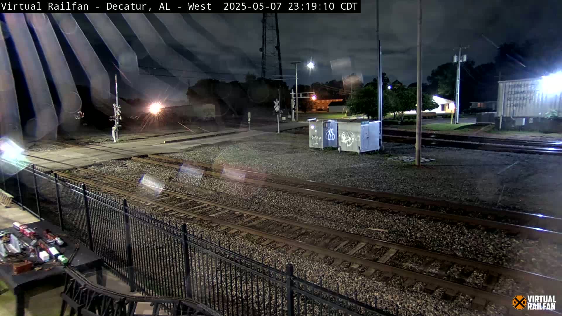 A nighttime view of railroad tracks and a nearby street, under a partly cloudy sky.