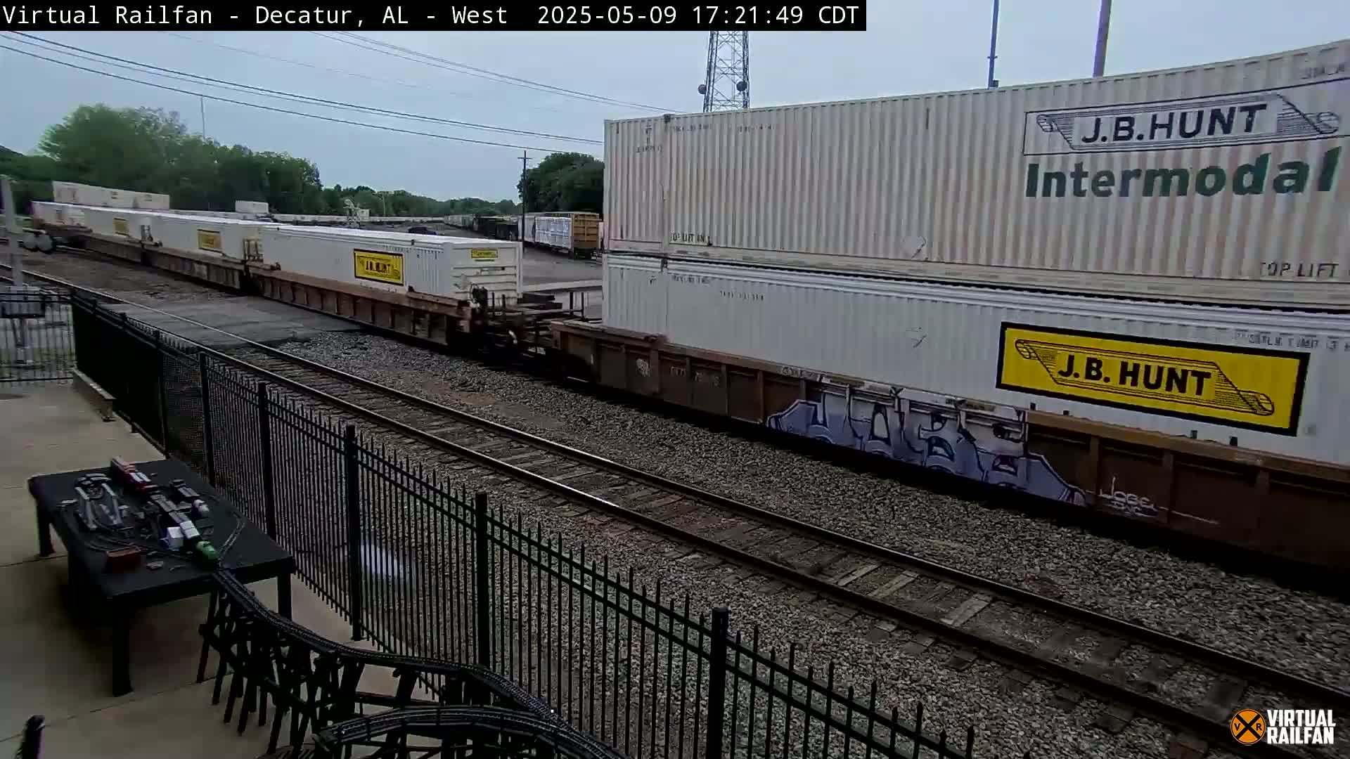 A long freight train carrying multiple white shipping containers passes by railroad tracks on an overcast day.