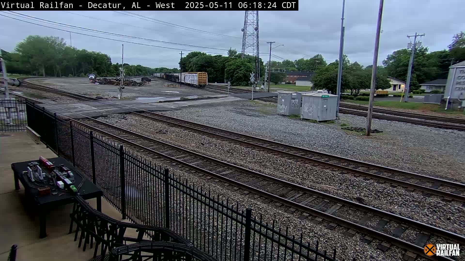 A mostly cloudy outdoor view of railroad tracks and switching yards, with a freight train partially visible in the distance.