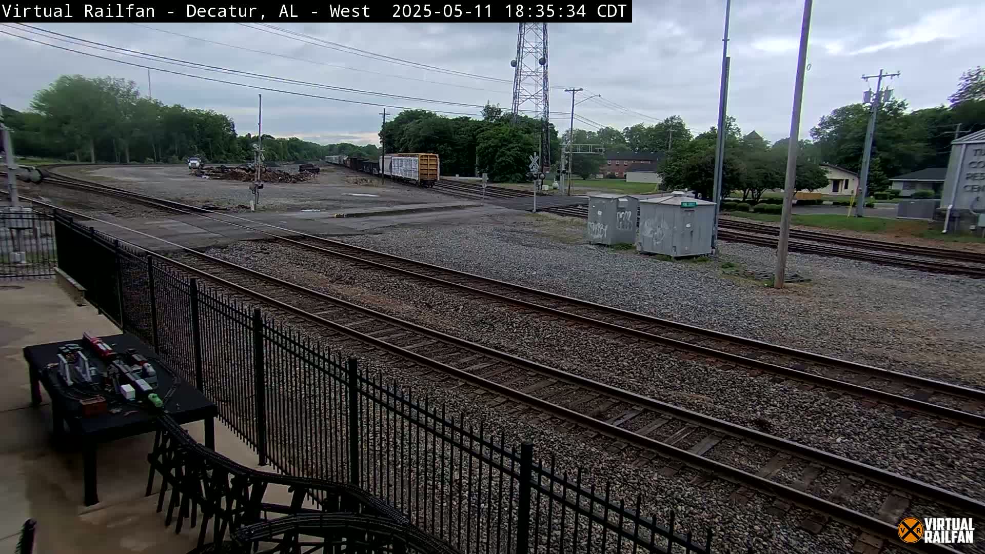 A train yard with multiple sets of tracks, a few rail cars, and some small buildings under an overcast sky.