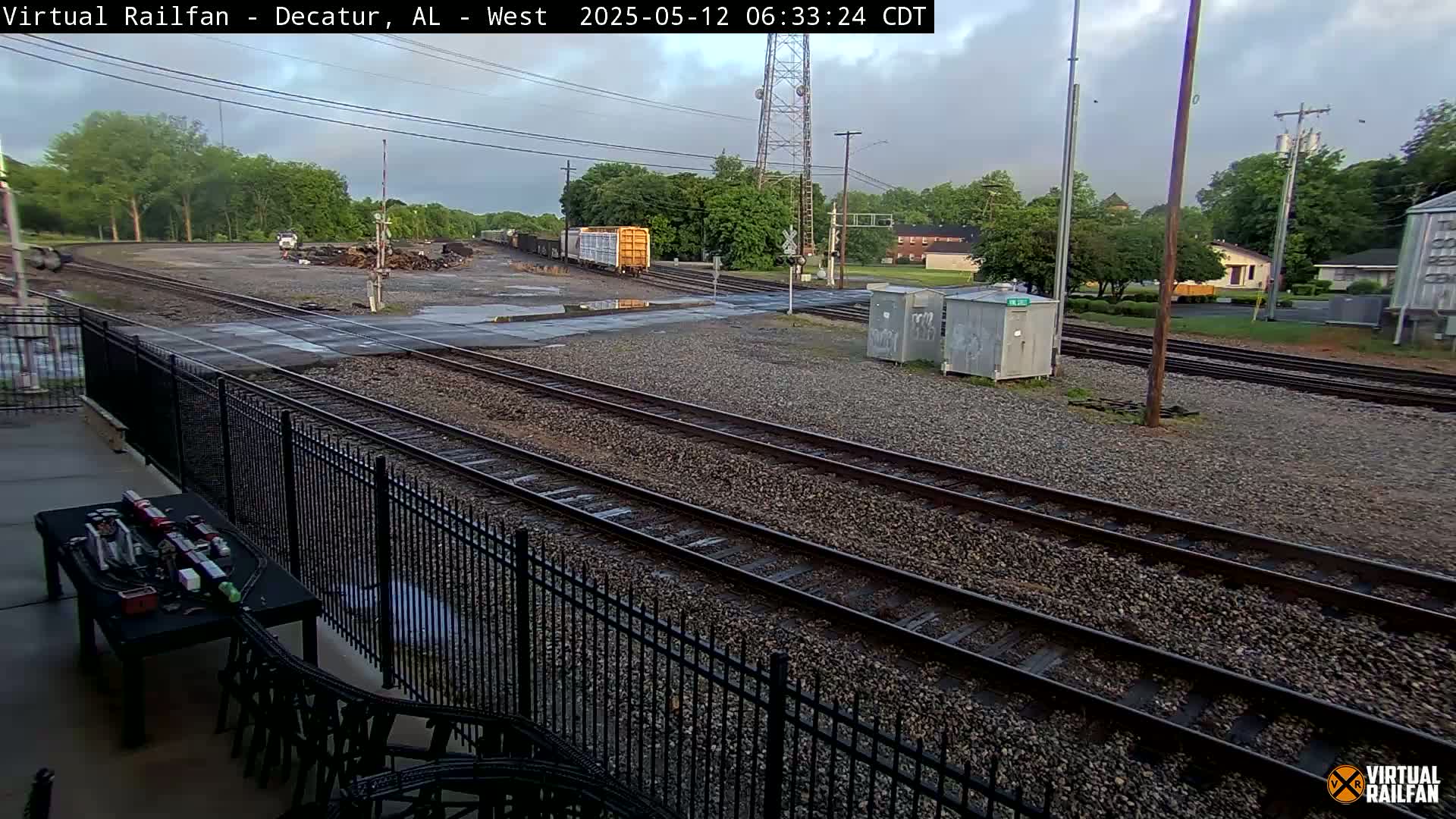 A view of railroad tracks and switching yards under an overcast sky, with a few buildings and trees visible in the background.