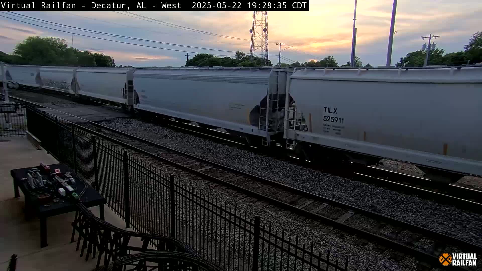 A long freight train of light gray hopper cars passes by under a twilight sky.