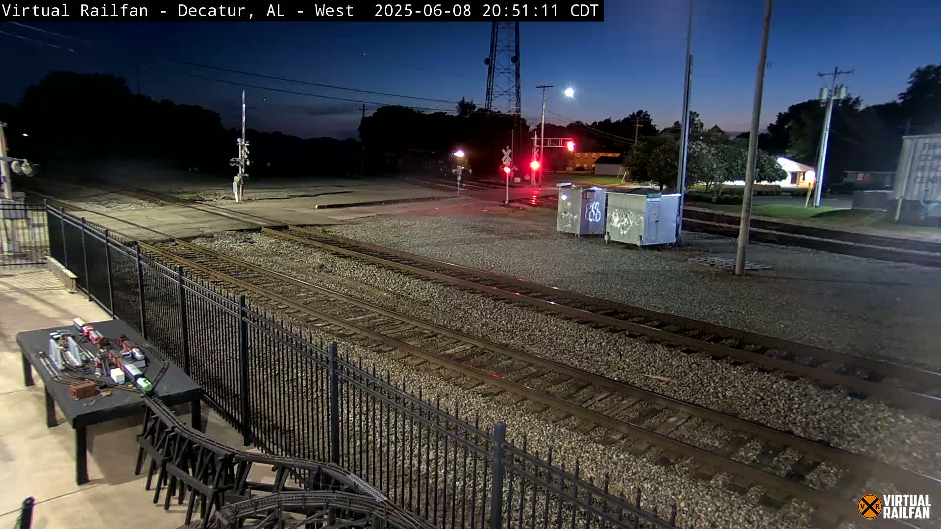 A nighttime view of railroad tracks and a crossing, under a twilight sky.