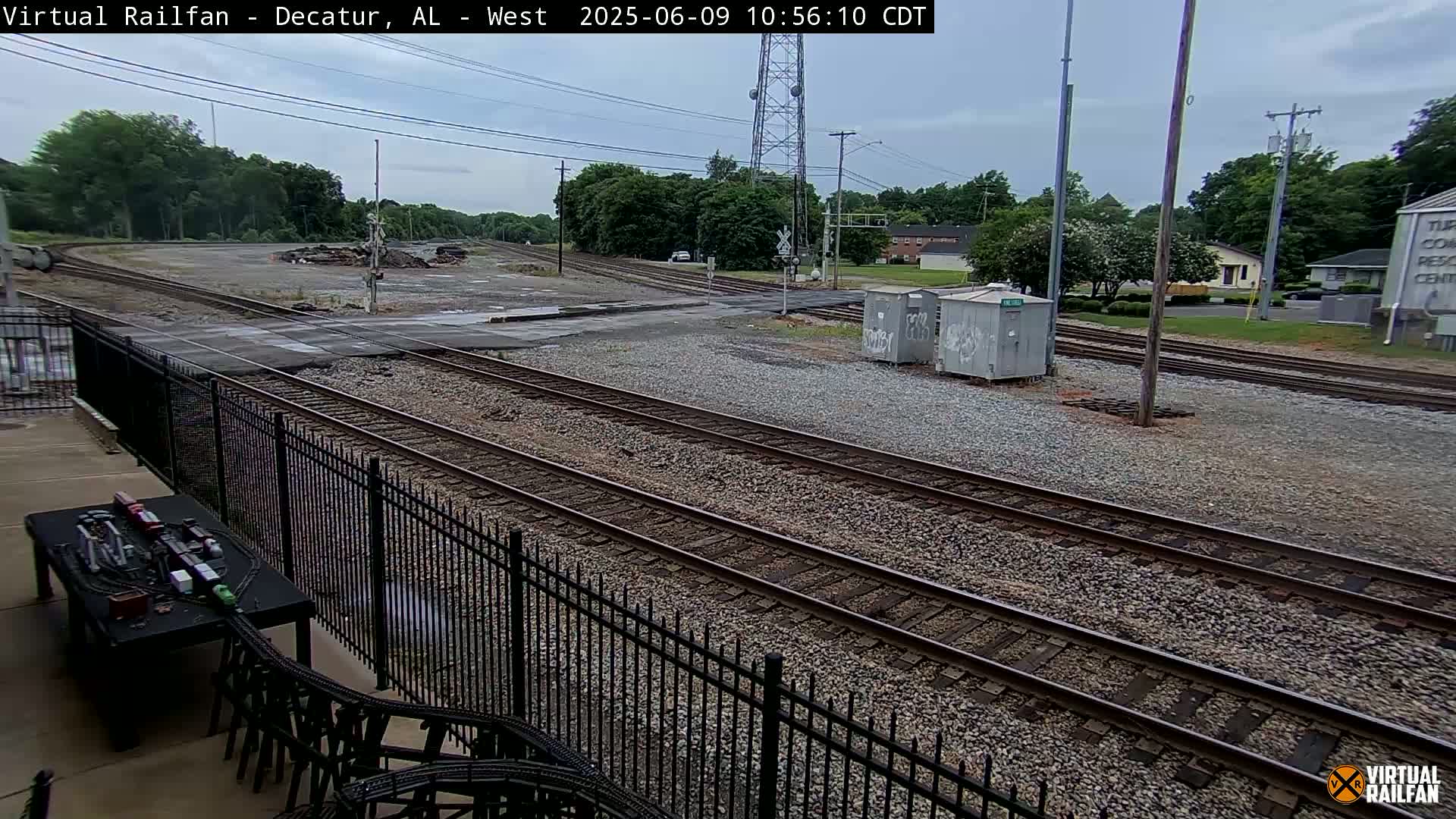 A view of railroad tracks on a partly cloudy day, with a model train set visible in the foreground.