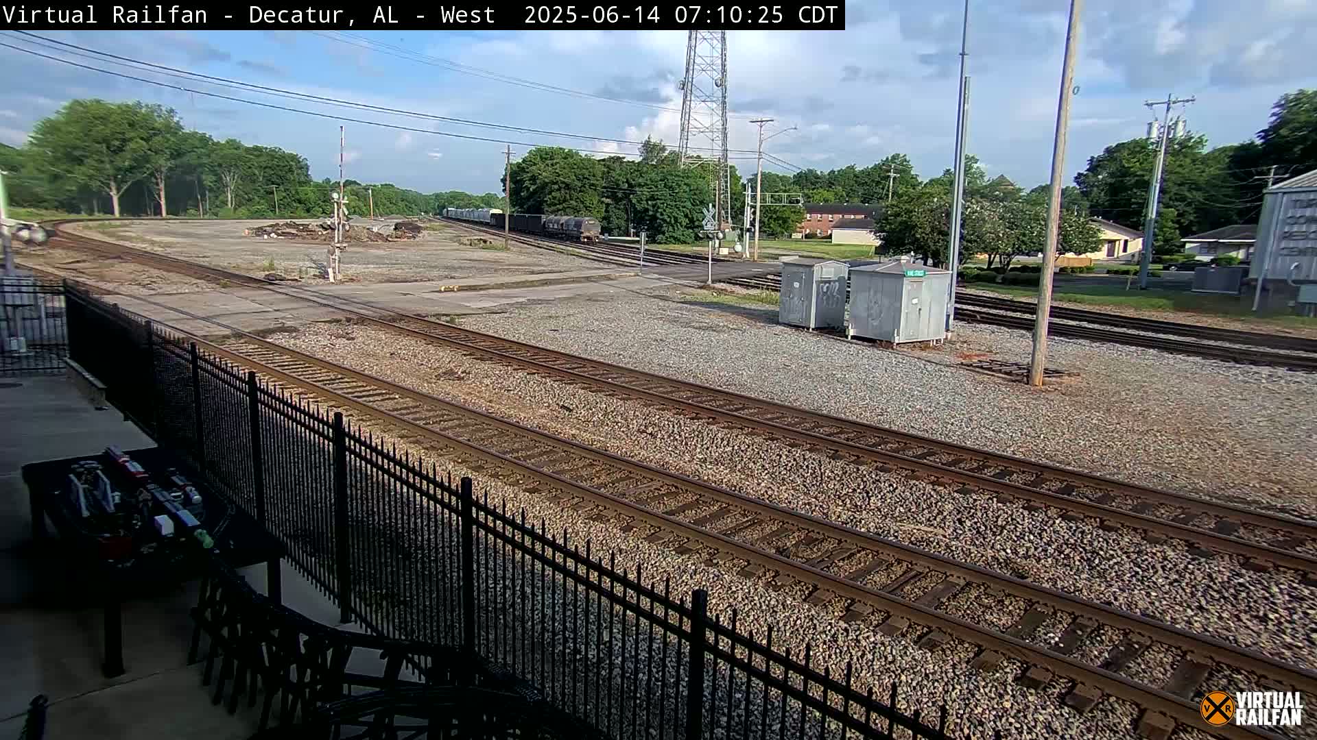 A freight train passes by a rail yard on a partly sunny day.