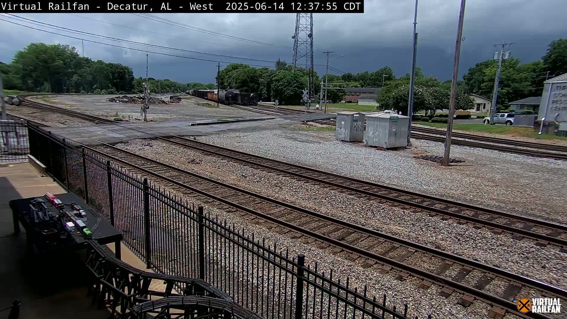 A railway yard with multiple train tracks, a few freight cars, and some utility boxes under a partly cloudy sky.