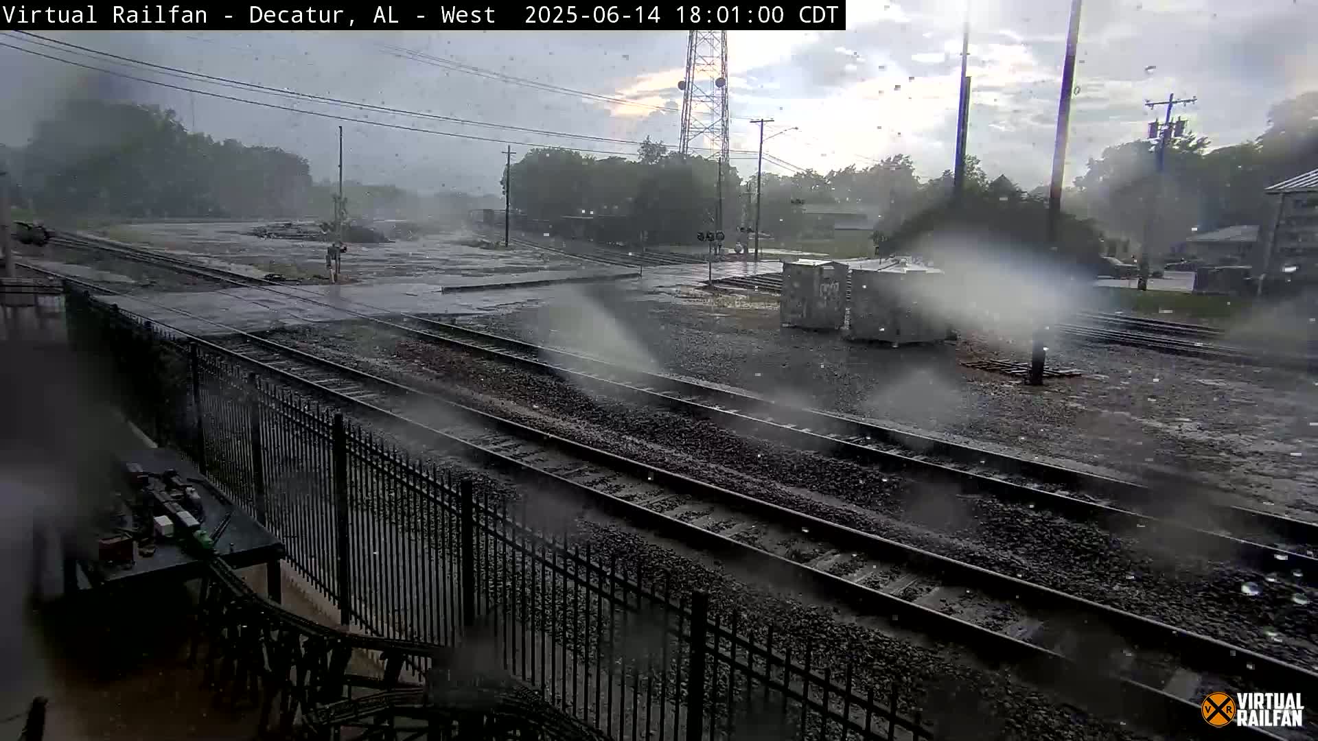 A railway yard with multiple train tracks, a few freight cars, and some utility boxes under a partly cloudy sky.