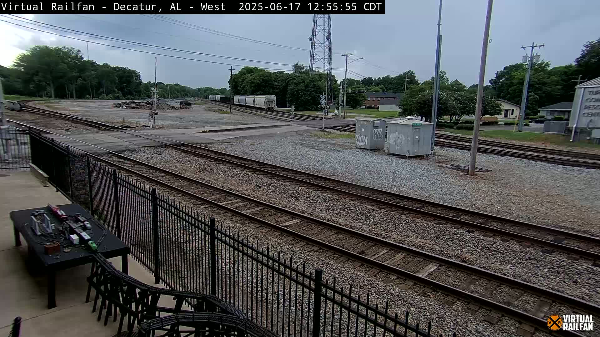 Multiple train tracks diverge near a fenced-in area, under an overcast sky.