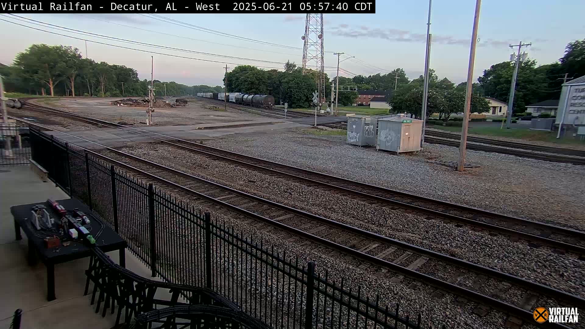A view of several train tracks in a gravel yard, with a train visible in the distance, under a partly cloudy sky.