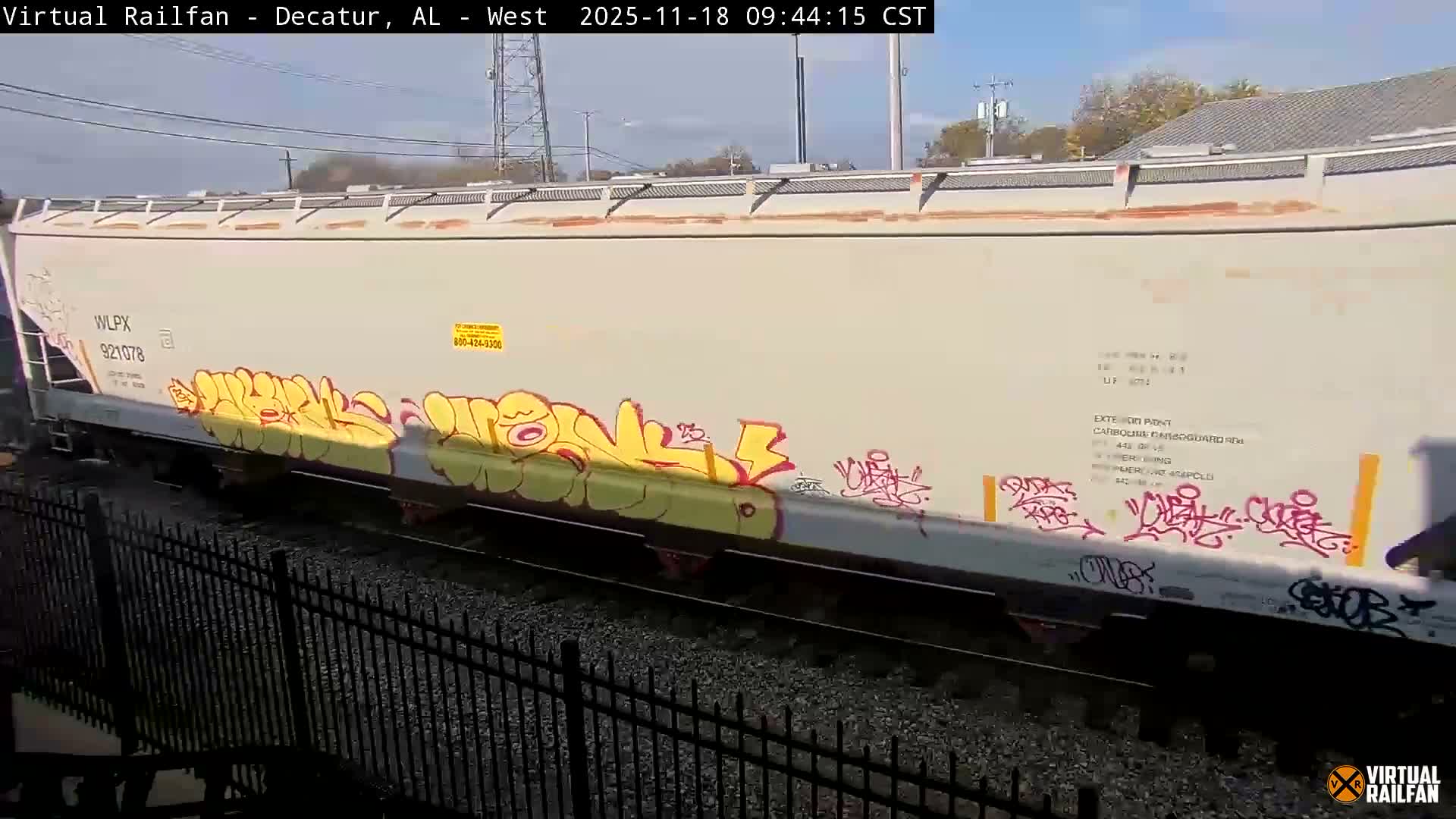 A nighttime view of railroad tracks, bordered by a black metal fence, with several containers nearby and a model train set on a table in the foreground.