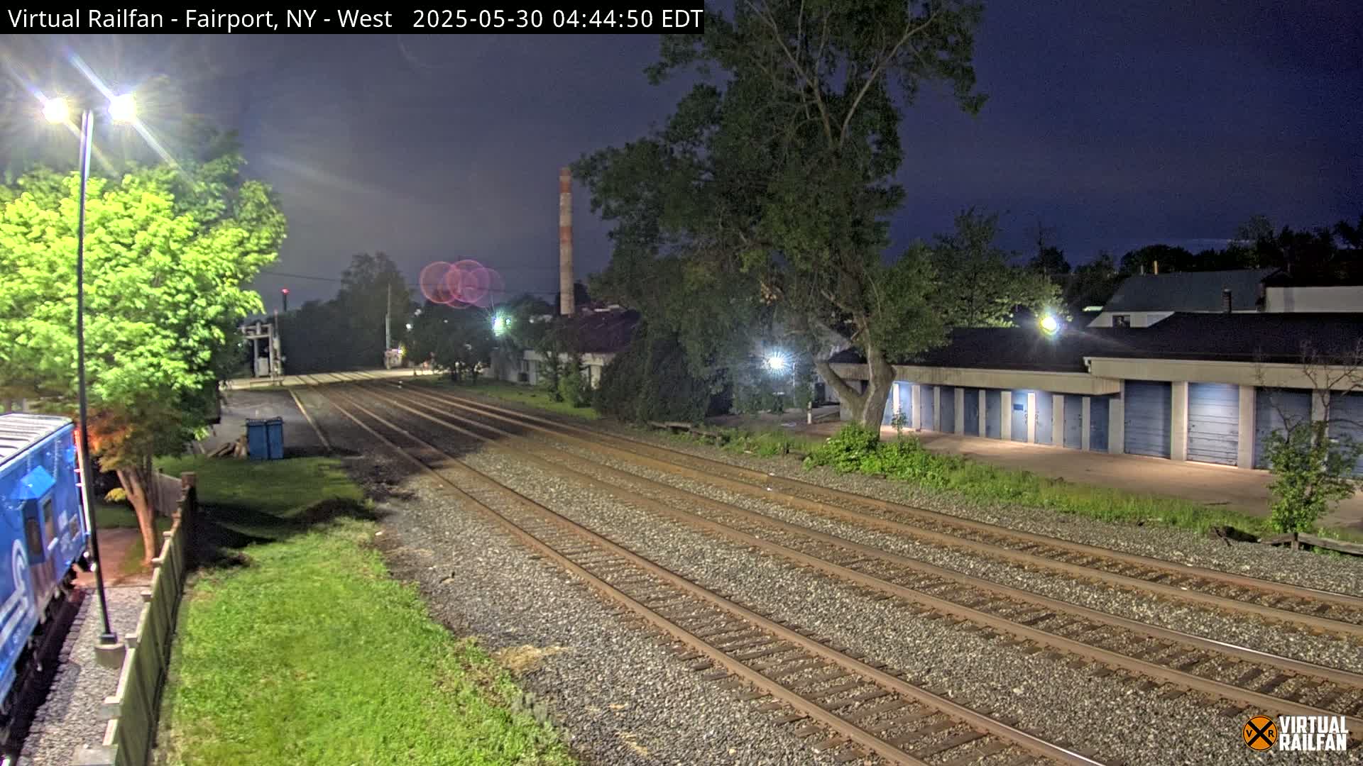Under a dark night sky, multiple train tracks stretch into the distance past a row of storage units and a partially visible train car.