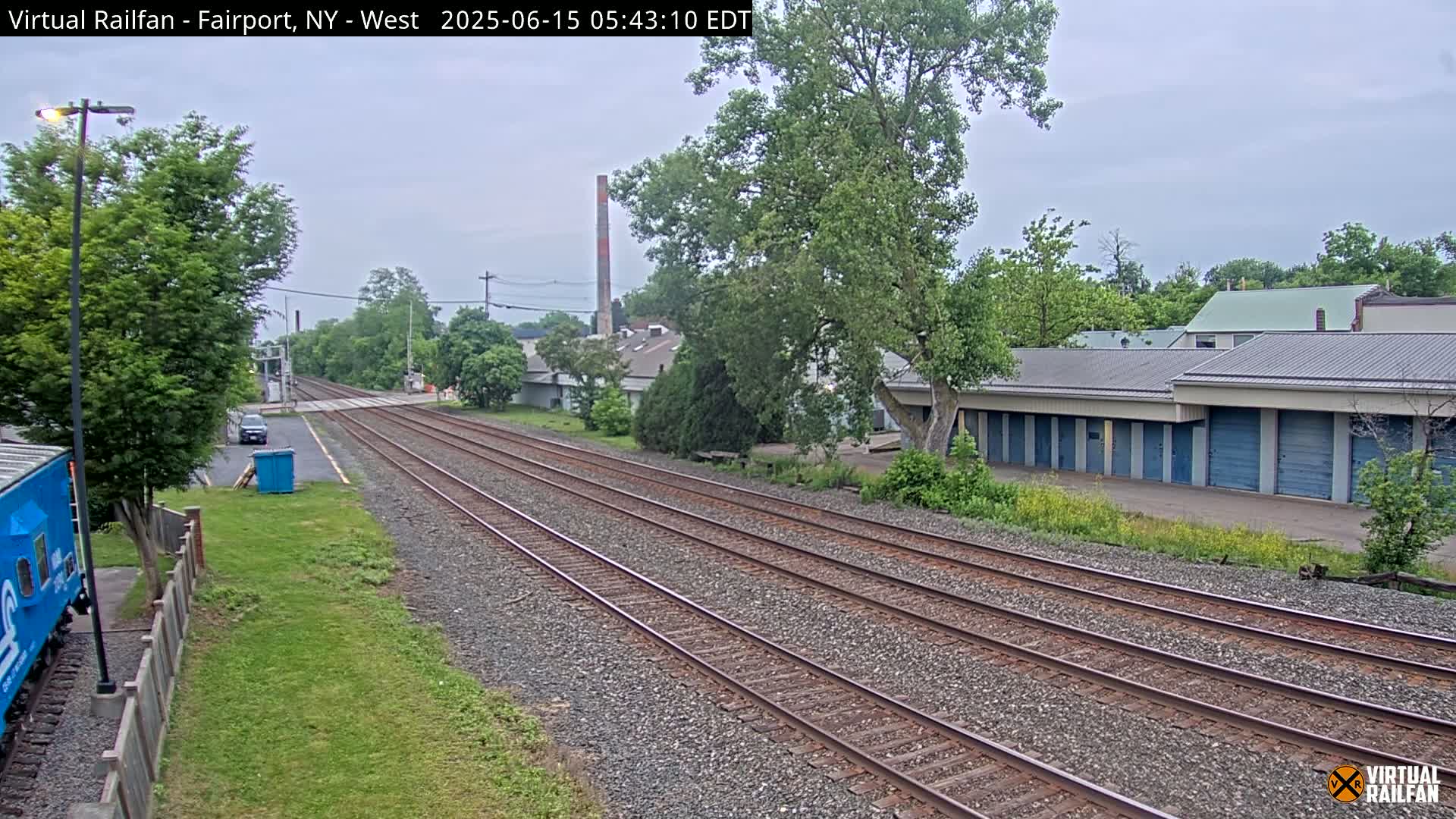 A view of railroad tracks extending into the distance under an overcast sky, passing alongside a row of storage units and some industrial buildings.