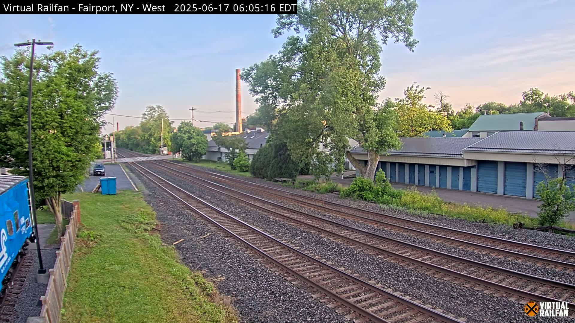 Multiple train tracks extend into the distance under a clear, light blue sky, passing alongside buildings and trees.