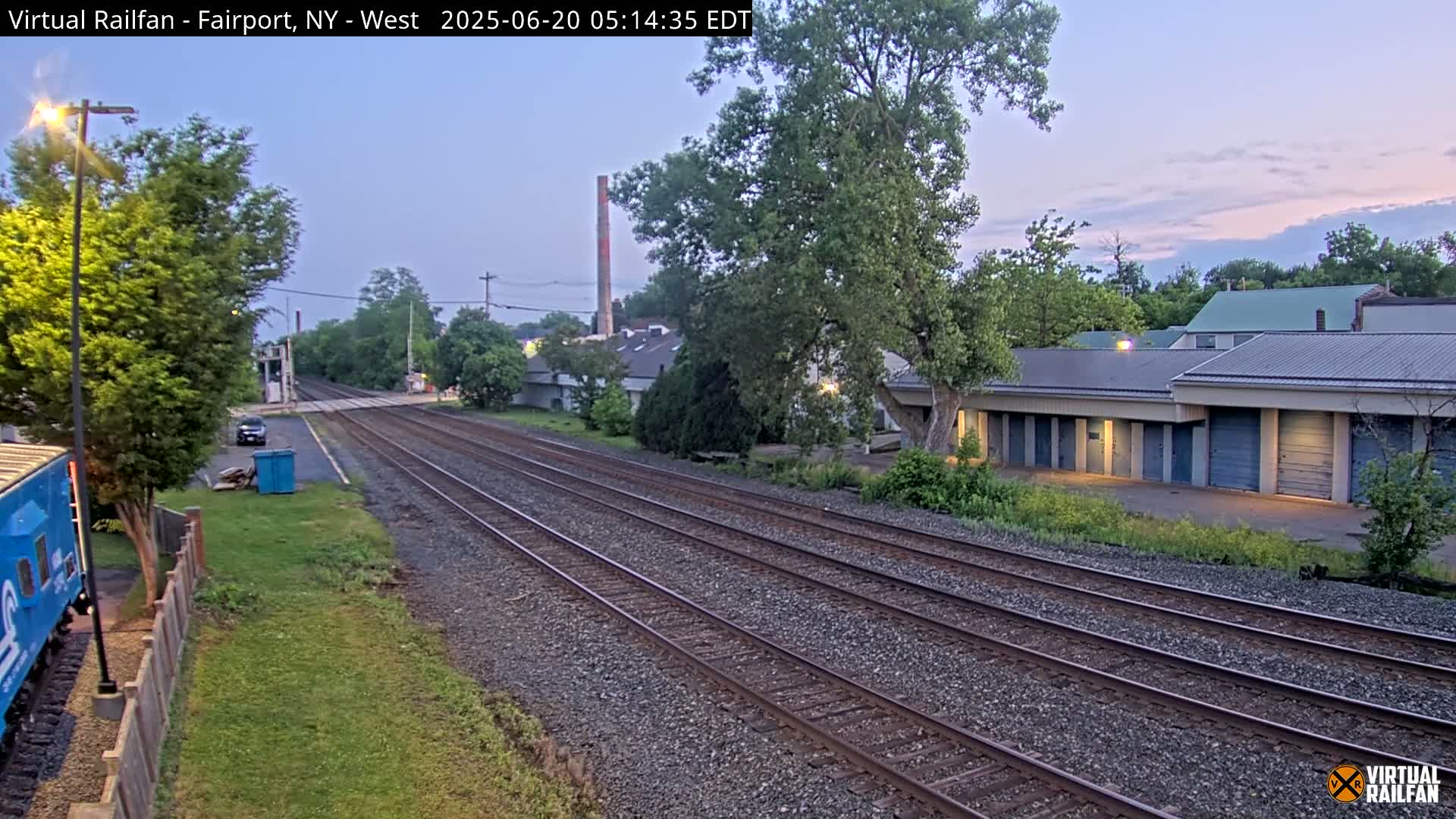 Train tracks stretch into the distance past a row of storage units under a twilight sky.