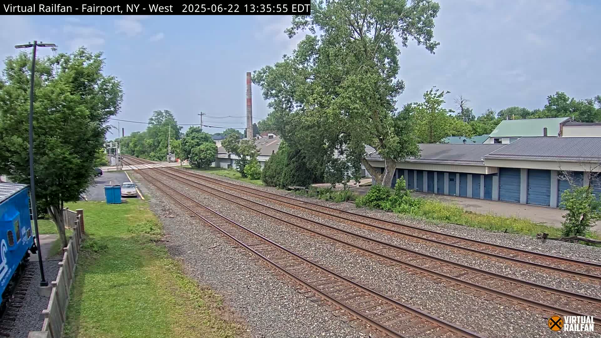 A view of train tracks extending into the distance on a partly sunny day, with buildings and trees lining either side.
