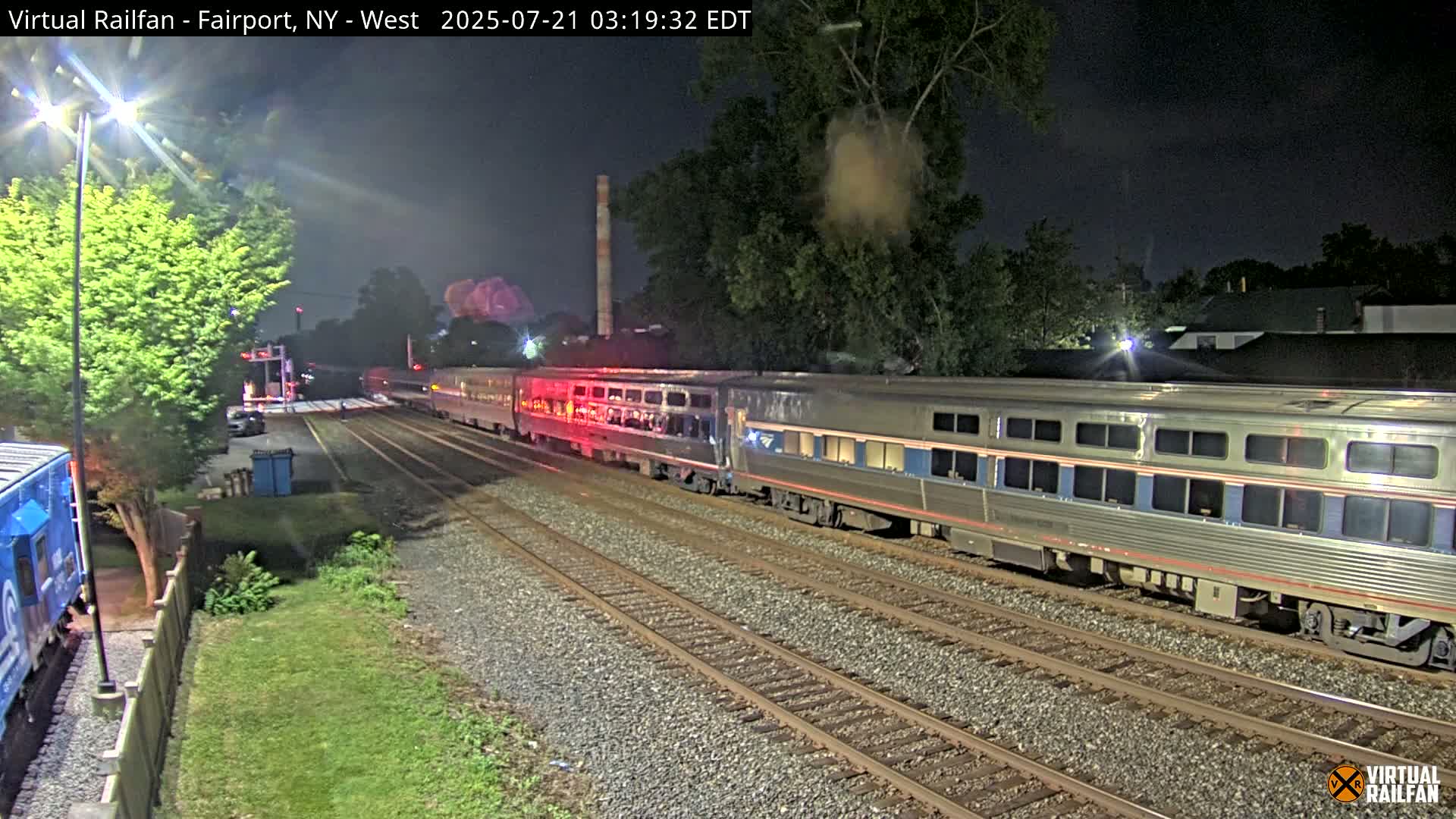 At night, a passenger train passes by another train on parallel tracks, under a dark sky.