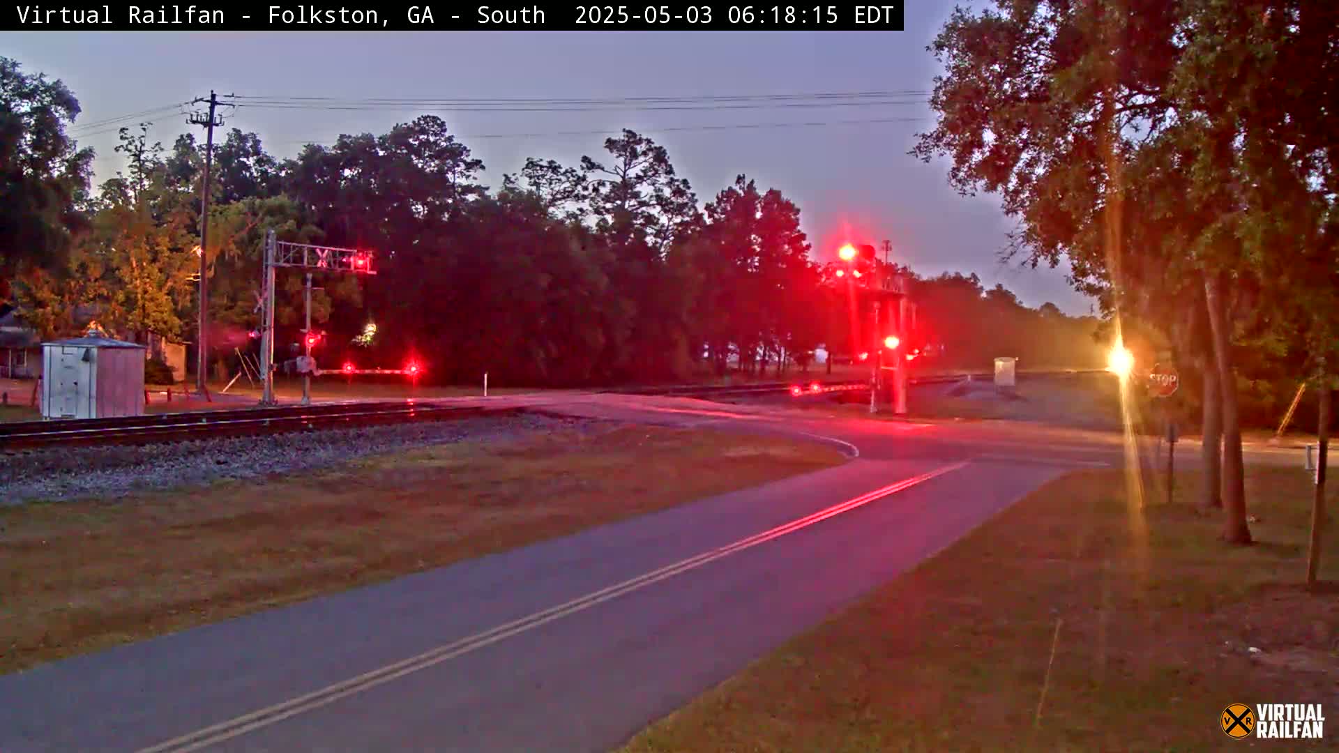 A road intersects a railroad crossing with flashing red lights under a twilight sky.