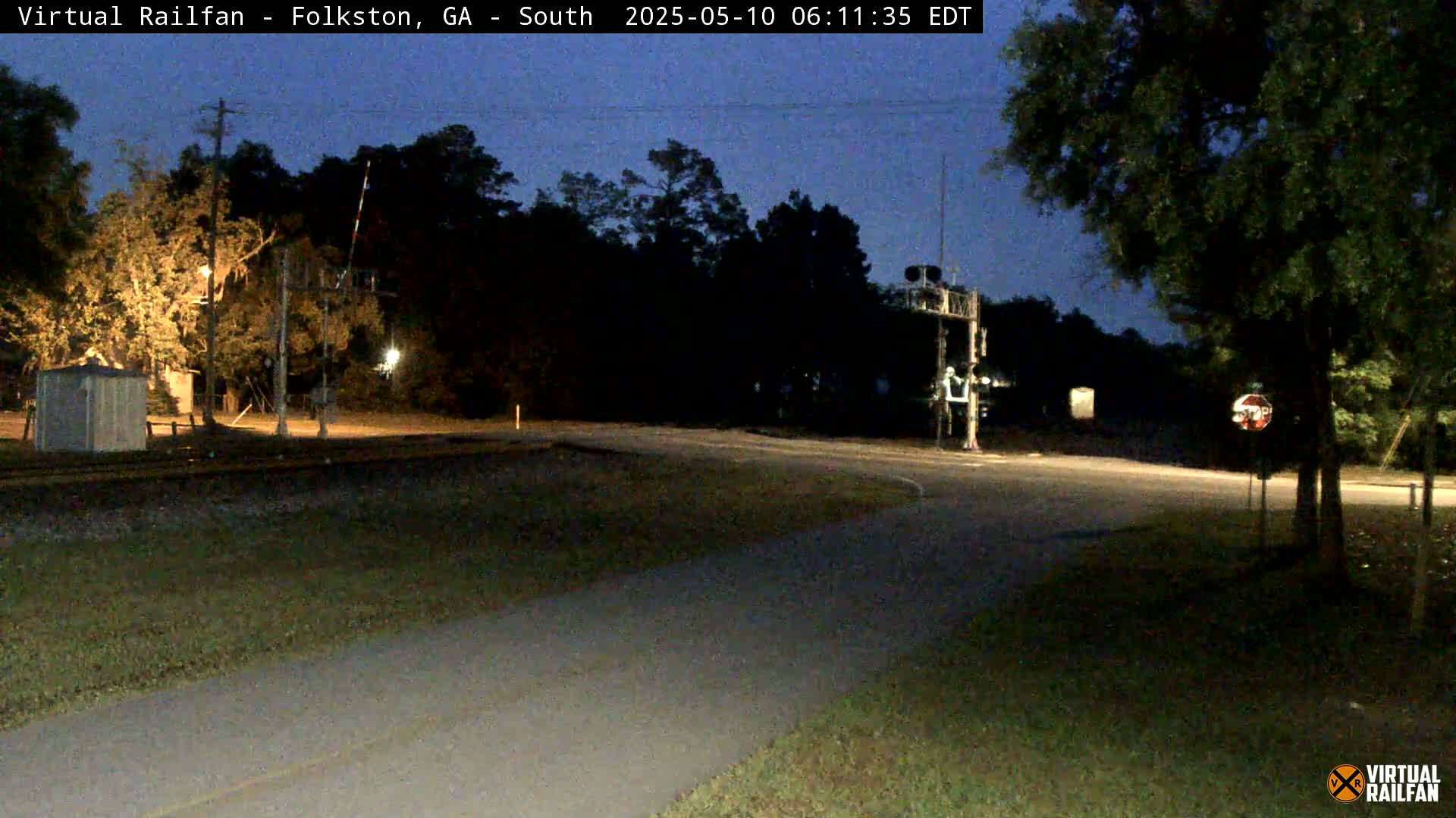 A nighttime view of a railroad crossing with a road intersecting, under a dark, clear sky.