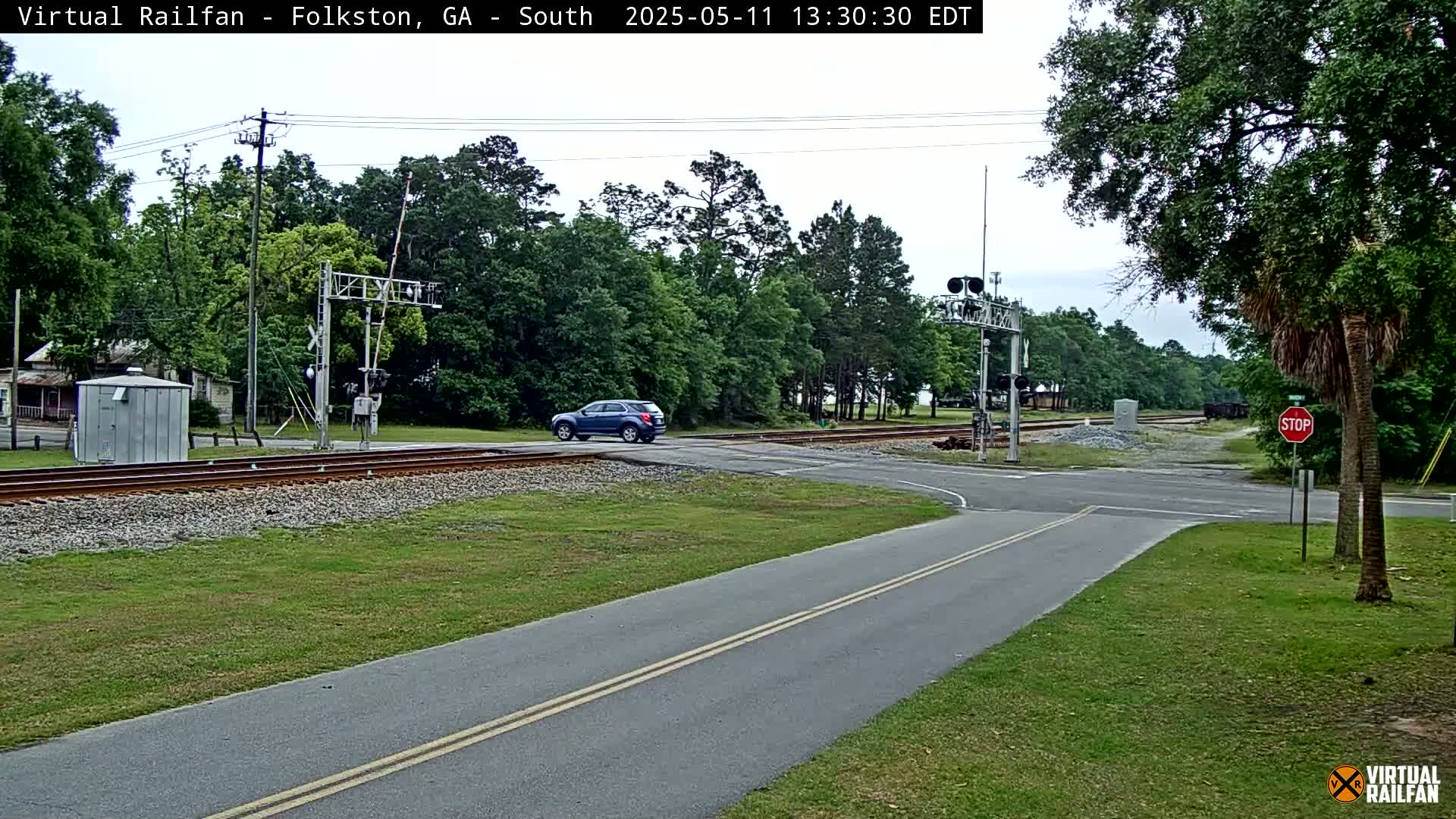 A dark-blue SUV crosses a railroad track at a road intersection in a wooded area under an overcast sky.
