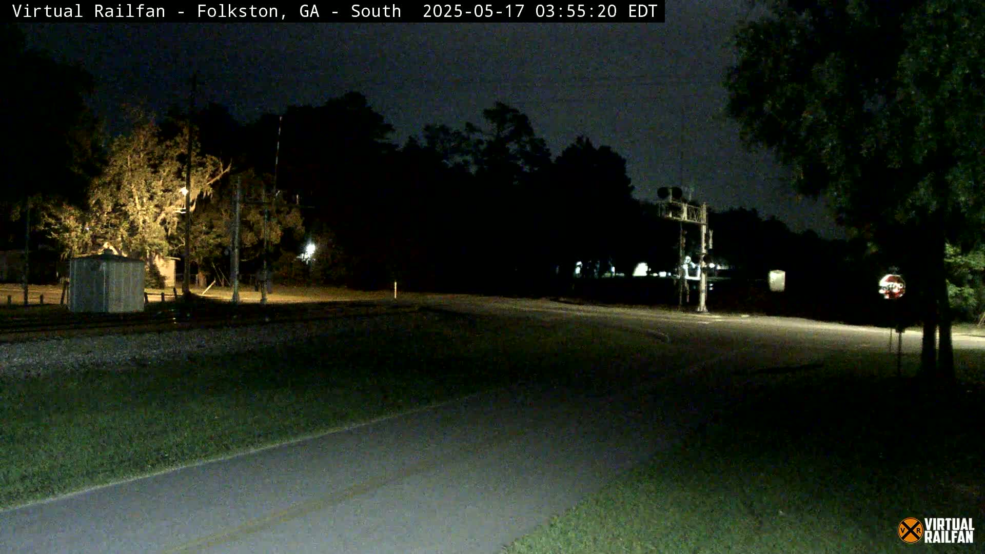 A nighttime view of a rural road intersection near a railroad crossing, under a dark sky.