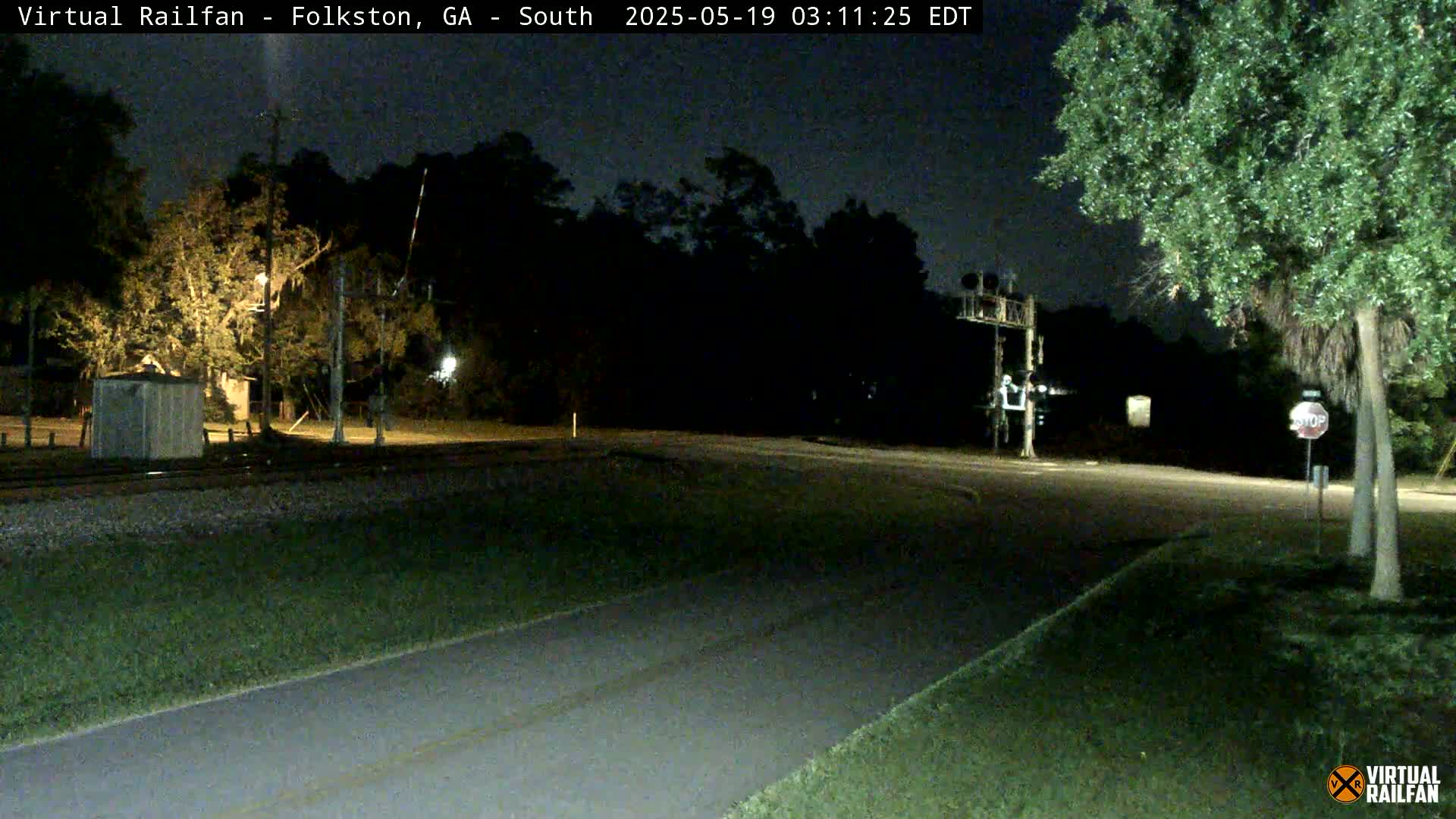 A nighttime view of a railroad crossing with a road intersecting, surrounded by trees under a dark sky.