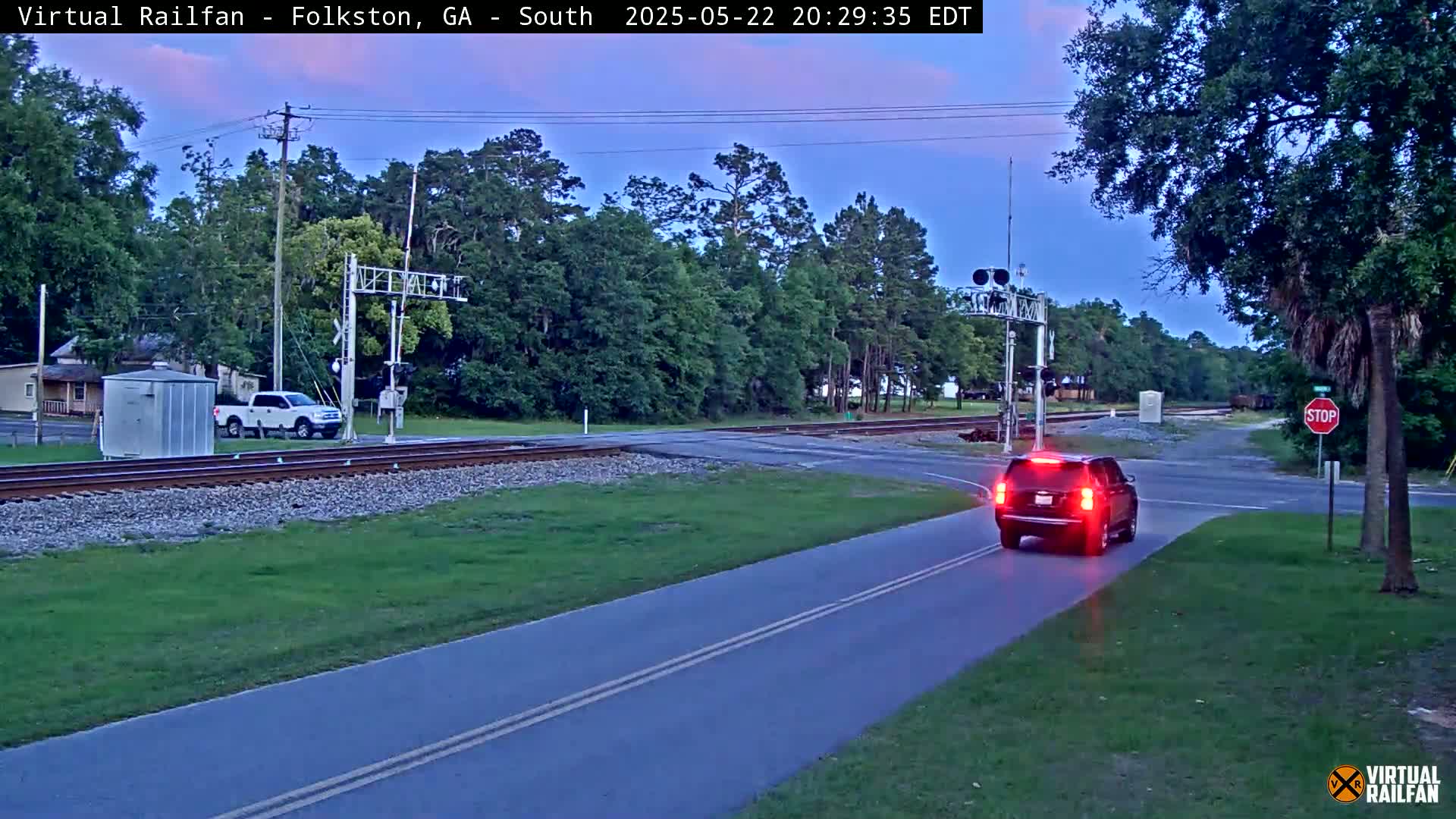 A dark-colored SUV drives across a road intersecting a railroad track under a twilight sky.
