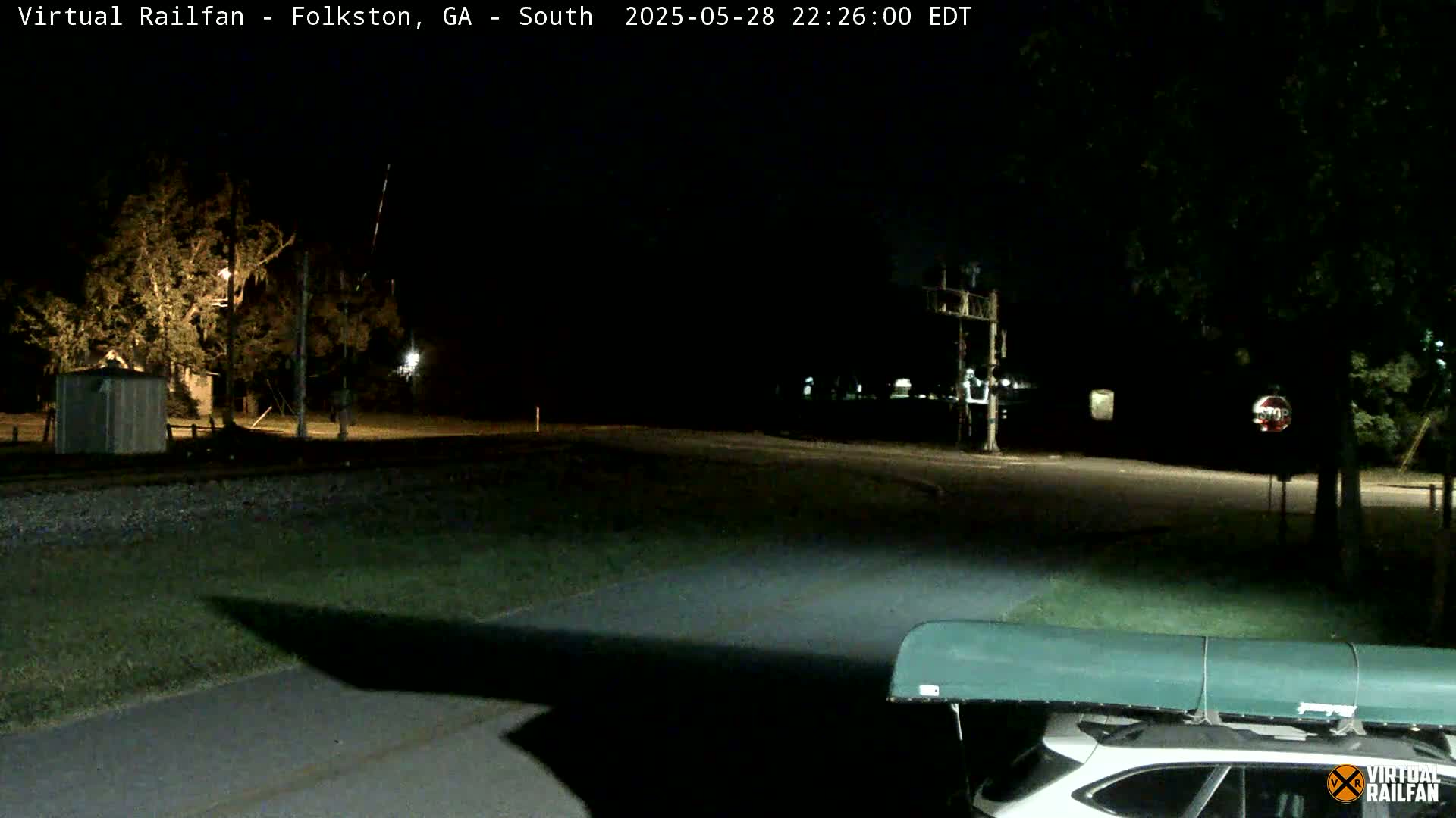 A nighttime view of a rural road intersection near a railroad crossing, with a vehicle and a canoe on its roof in the foreground.
