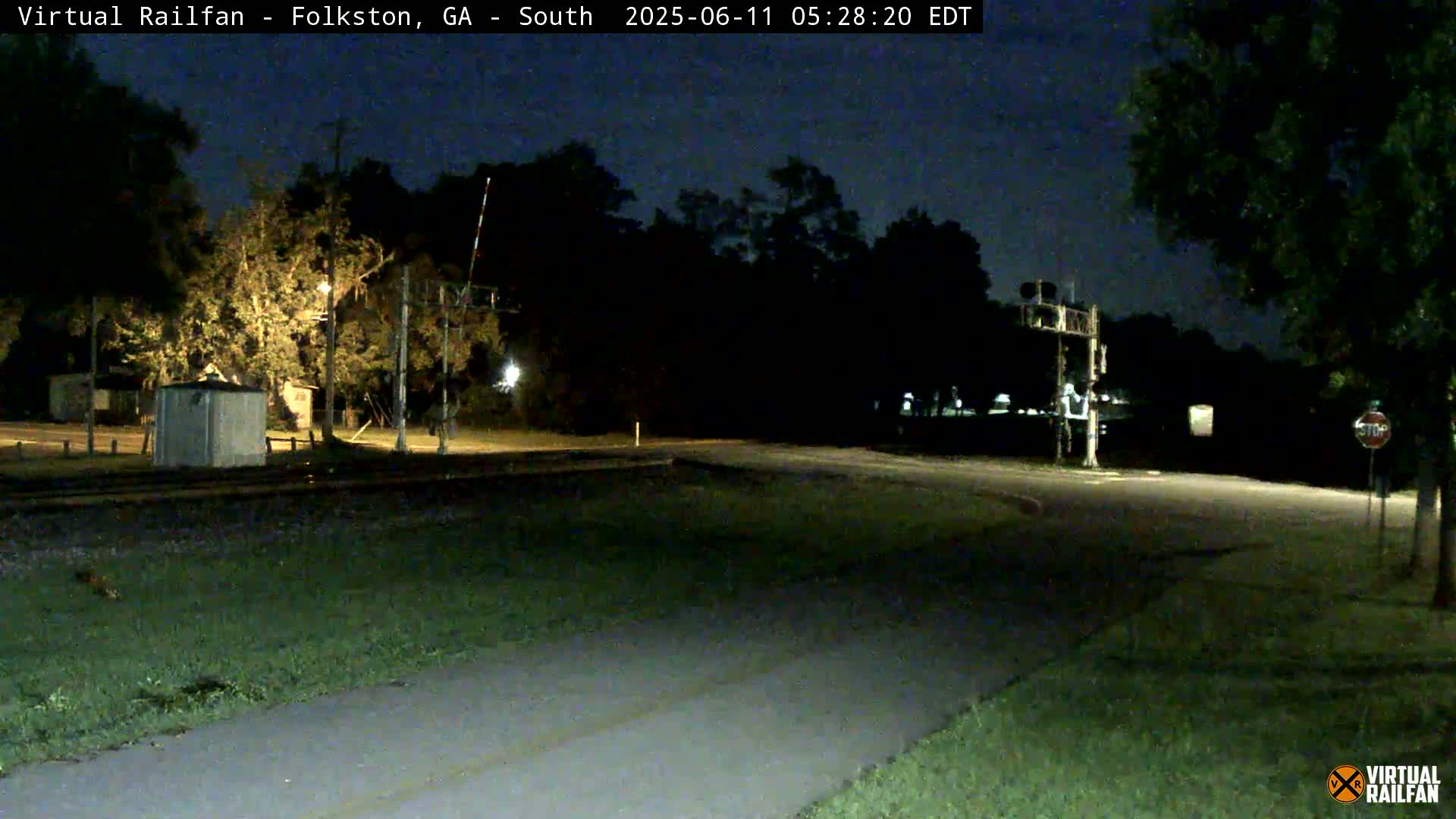 A nighttime view of a railroad crossing with a road intersecting it, surrounded by trees under a dark sky.