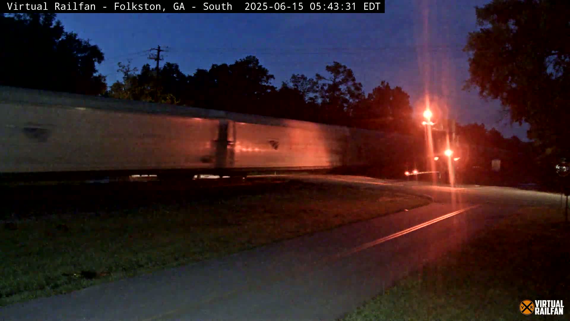 A long freight train passes by at night under a dark, clear sky near a road with a bike path.