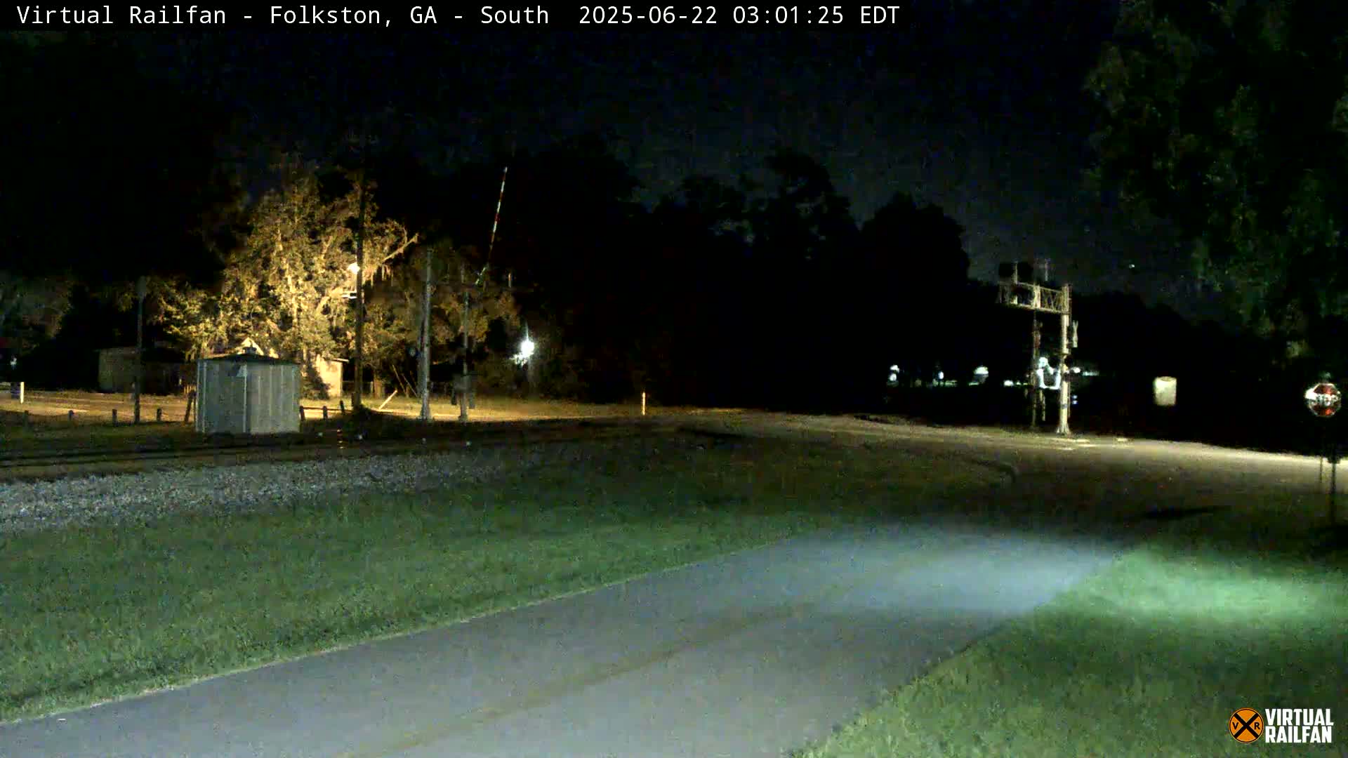 A nighttime view of a railroad crossing with a paved path leading to it, under a clear sky.