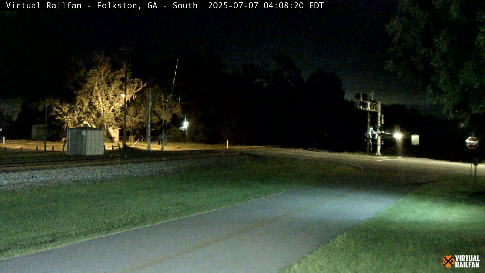 A nighttime view of a railroad crossing with a road intersecting it, under a dark, clear sky.
