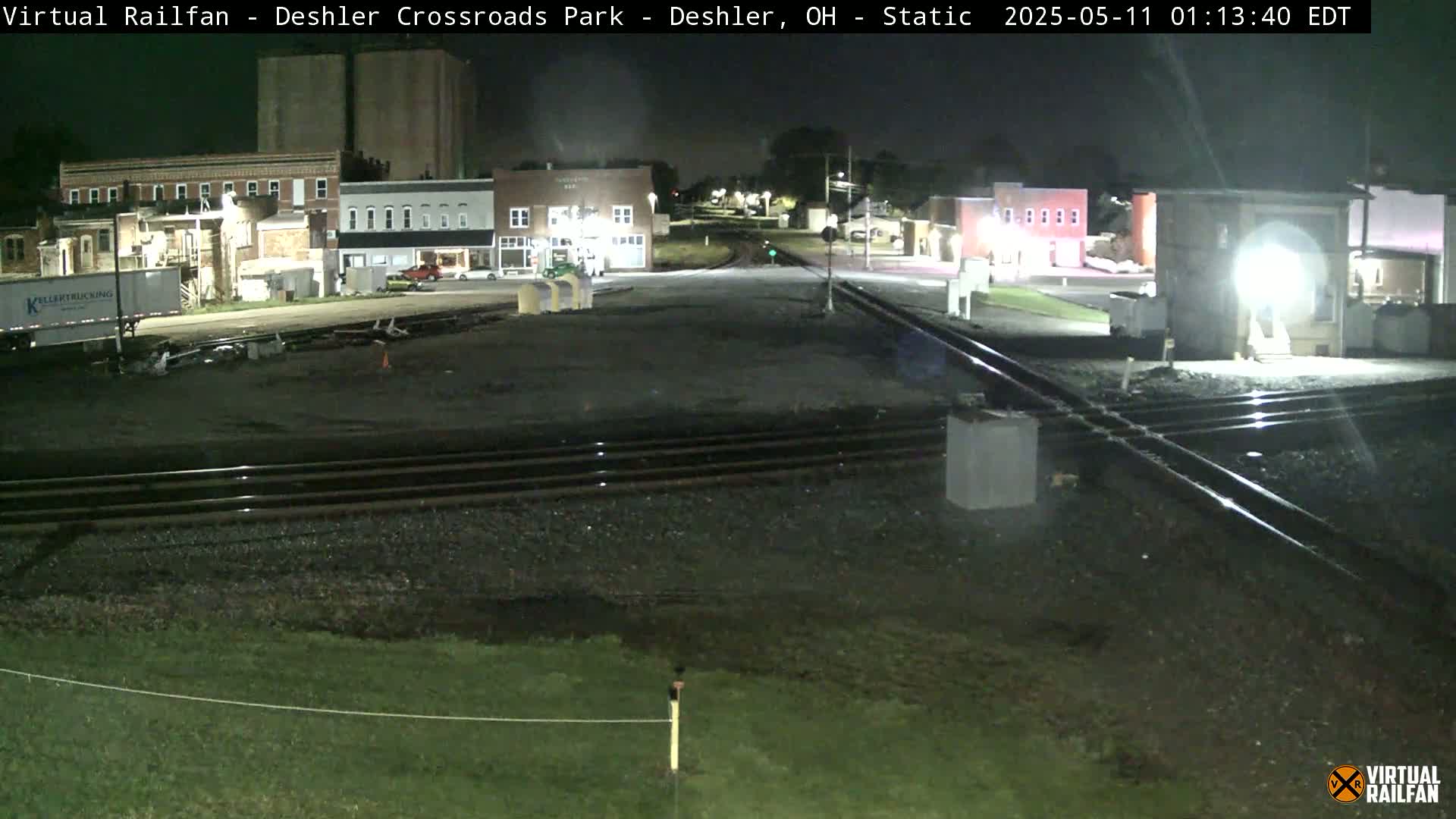At night, railroad tracks intersect near a small town with buildings under low light conditions.
