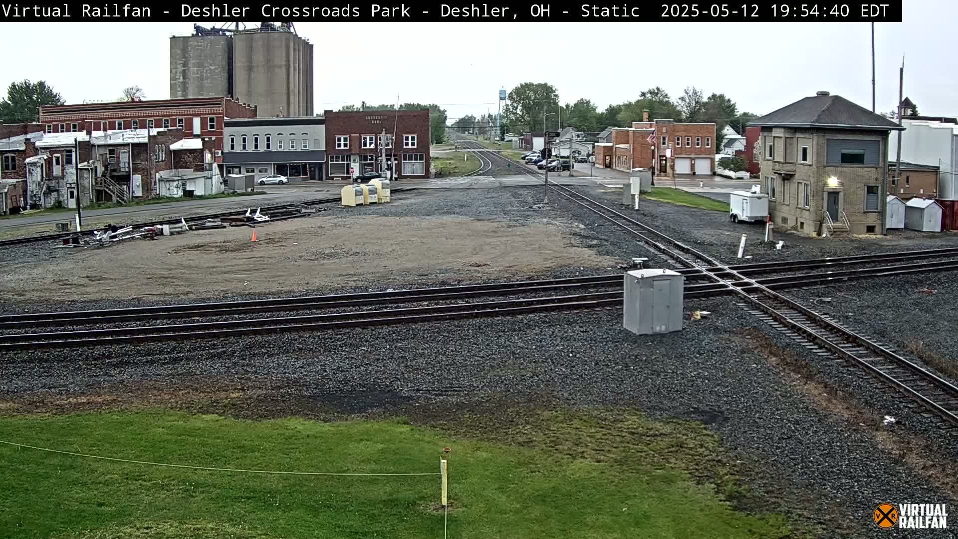 A railroad crossing in a small town on an overcast day, with several buildings and a railway signal tower visible.