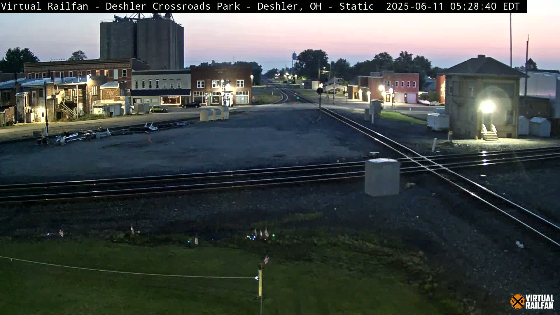 A small town with railroad tracks intersecting in front of several brick buildings at dawn.