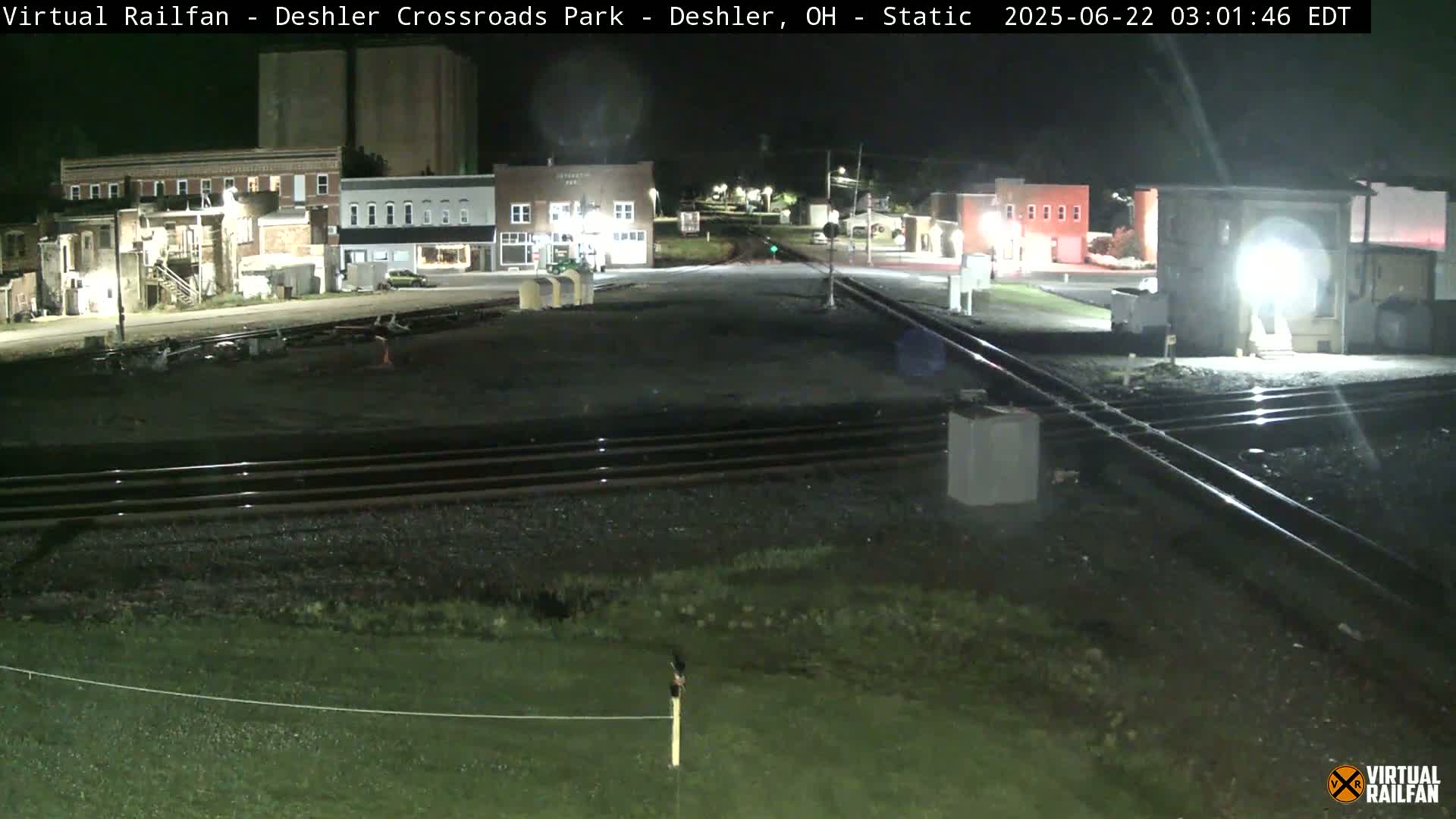 A nighttime view of a railroad crossing near buildings in a small town.