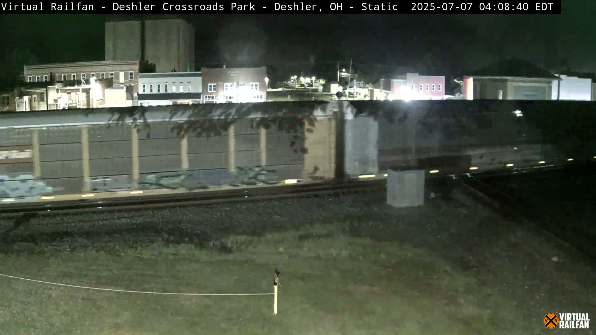A long freight train passes by at night in front of a small town.