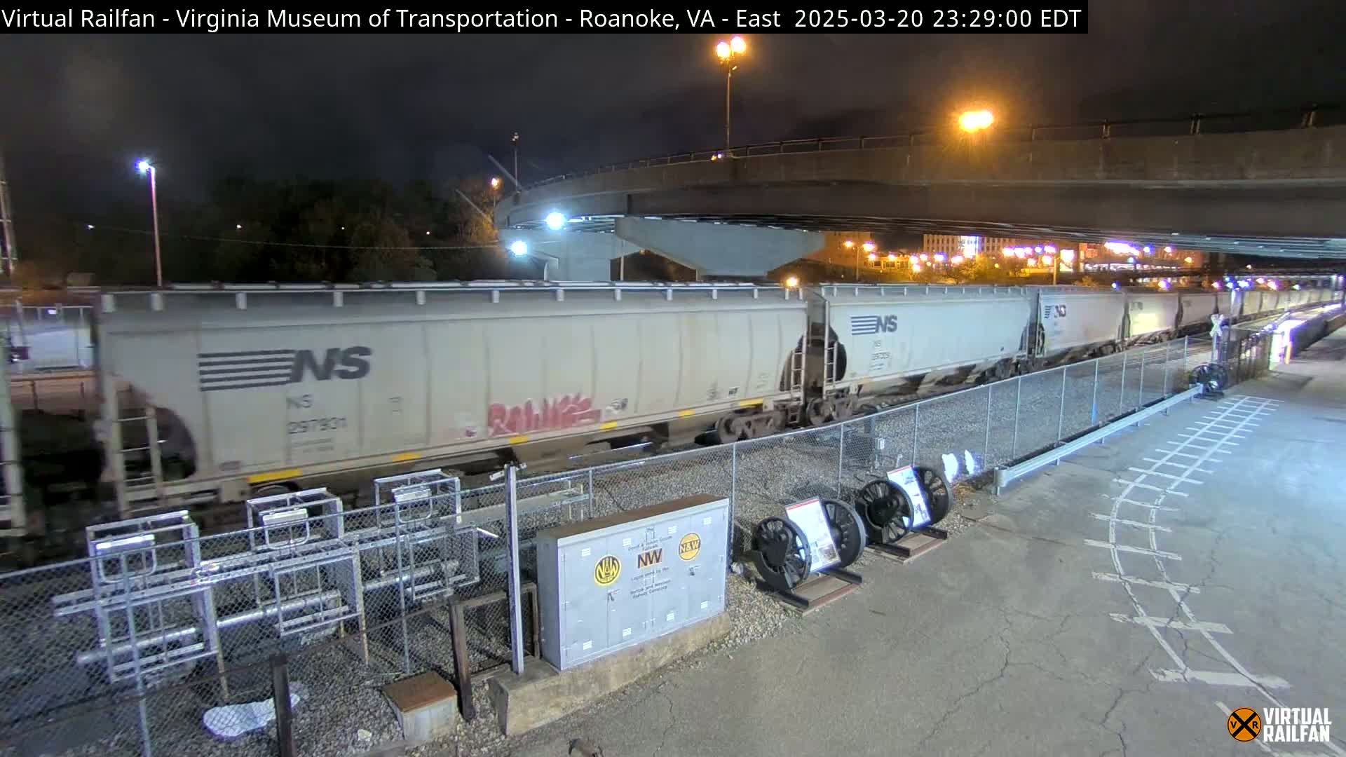 A long freight train passes under a highway overpass at night.