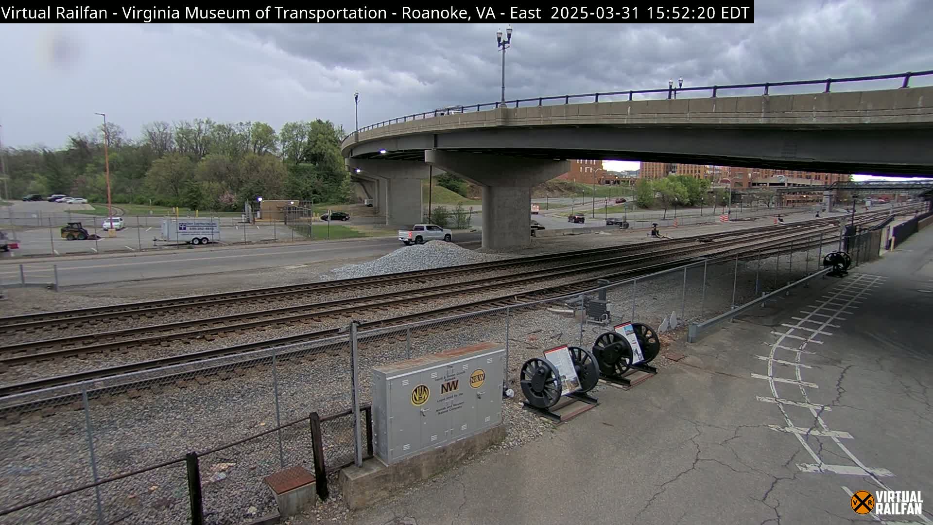 A partly cloudy day shows a view of railroad tracks, a road, and a bridge; a small pile of gravel sits near the tracks.