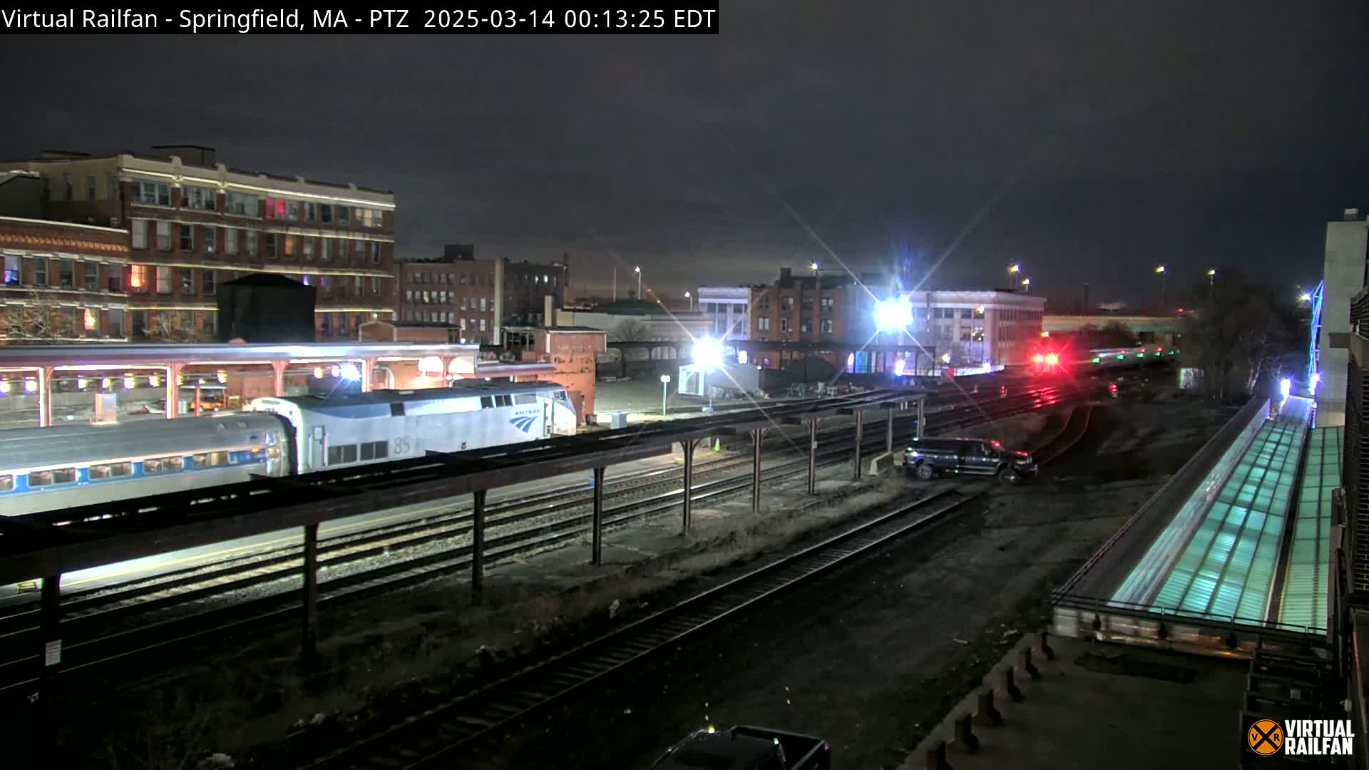 A passenger train is stopped at a nighttime station, with several cars visible, under a dark sky.
