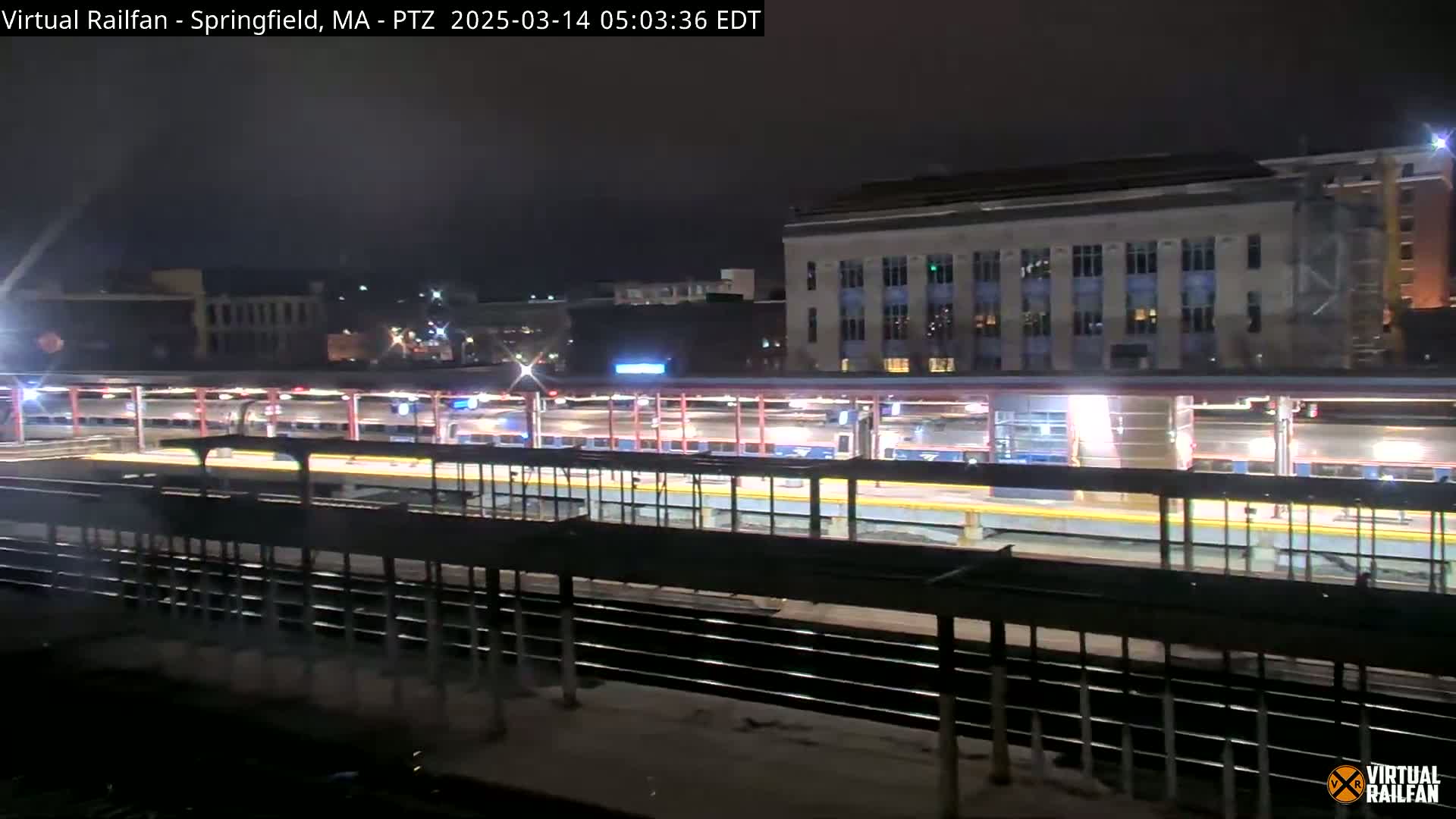 A nighttime view of a train station with several passenger trains at the platform under a dark sky.
