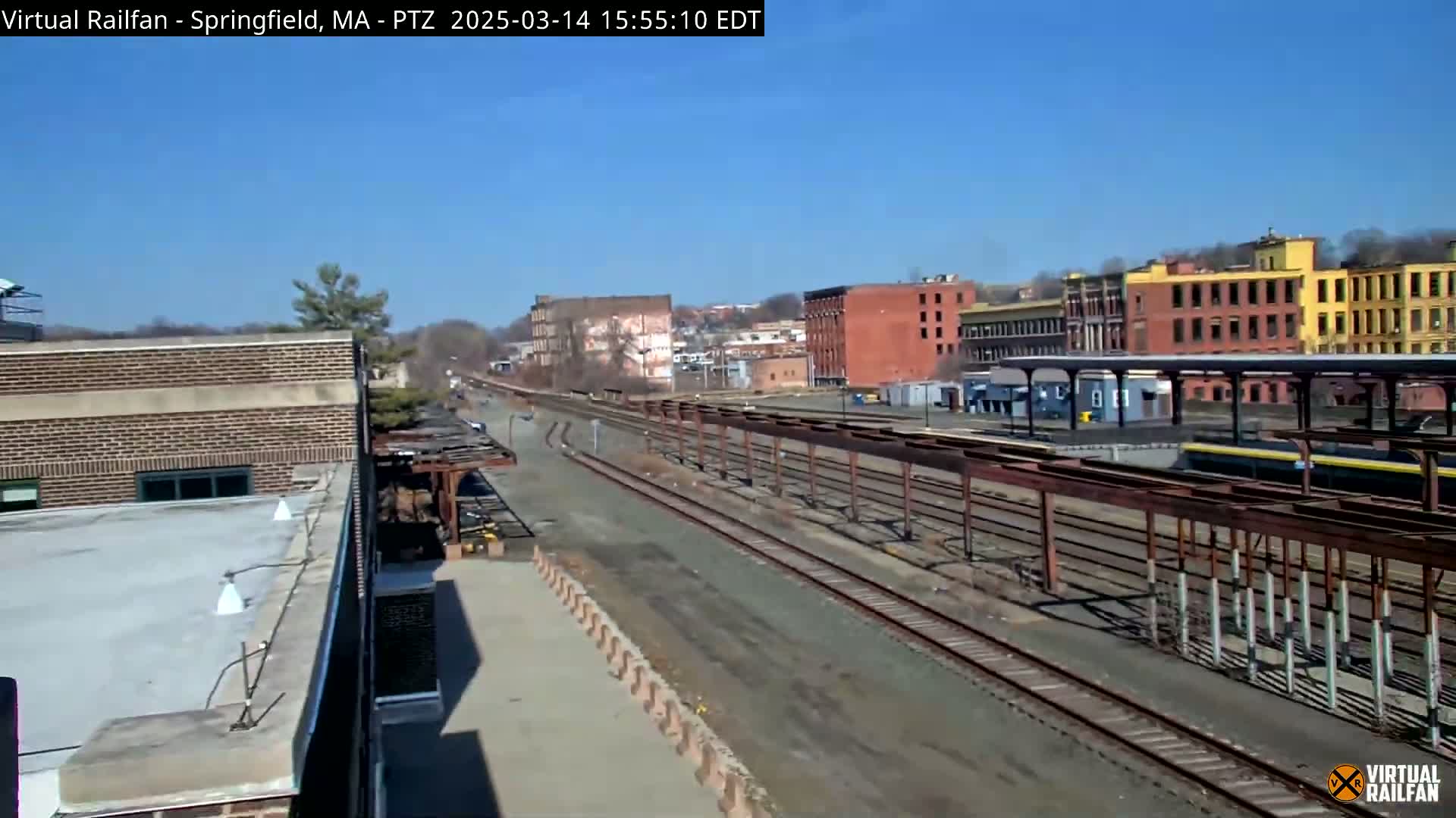 A long view of train tracks stretches out from a brick building under a clear blue sky.